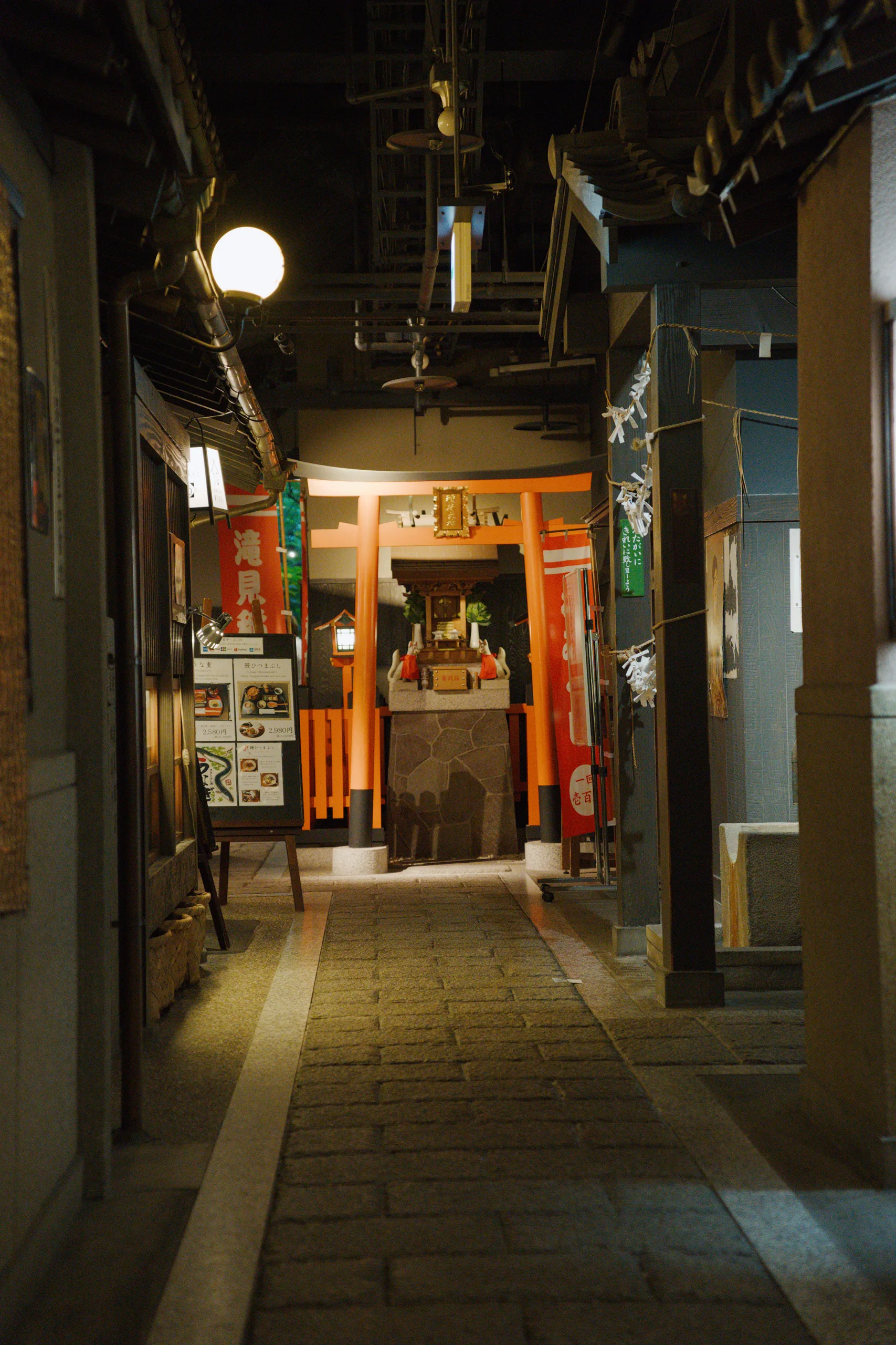 A narrow alley lined with shops, one with an orange-lit entrance, at night.