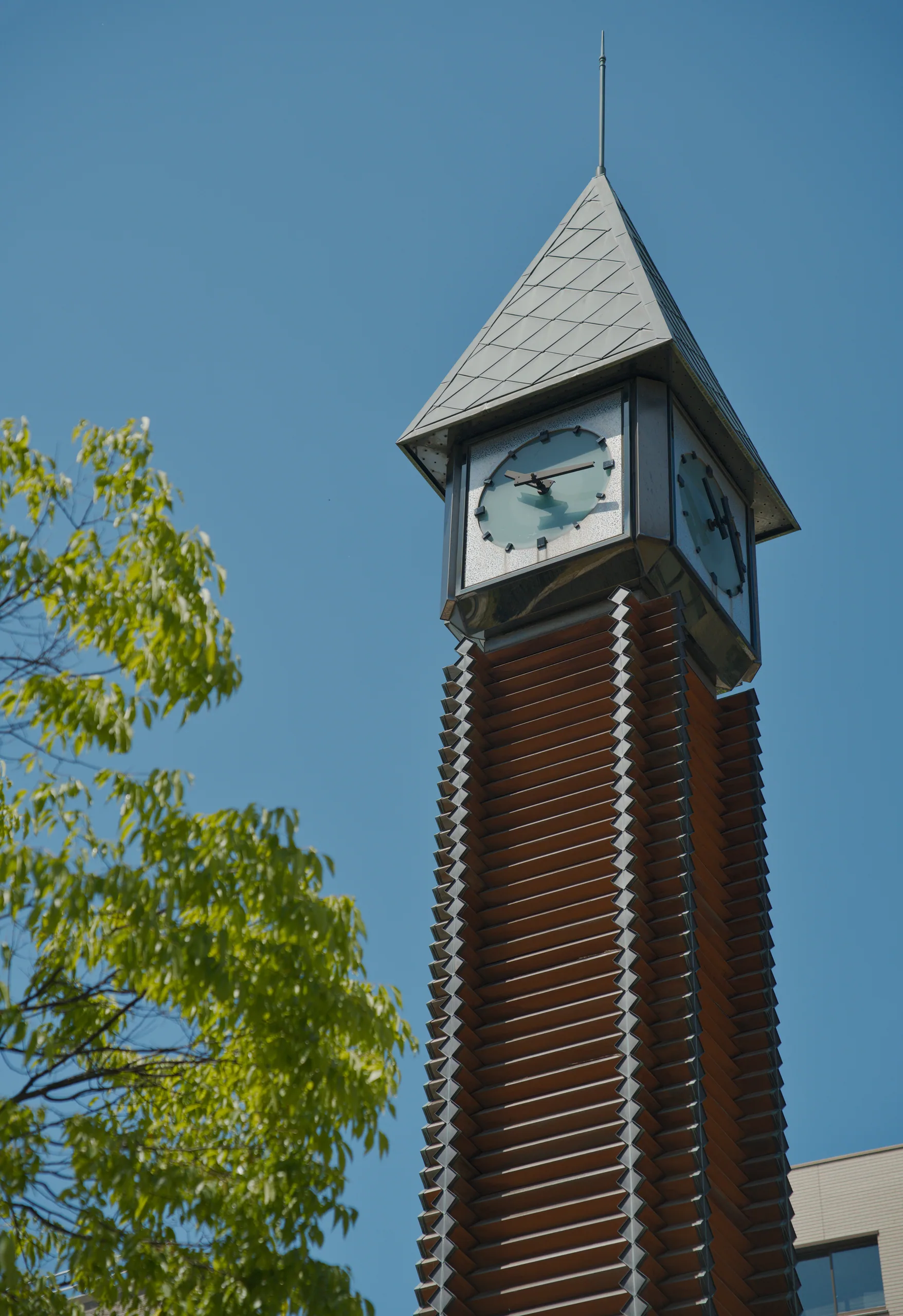 A brick clock tower with a peaked roof and clock face stands against clear blue sky.