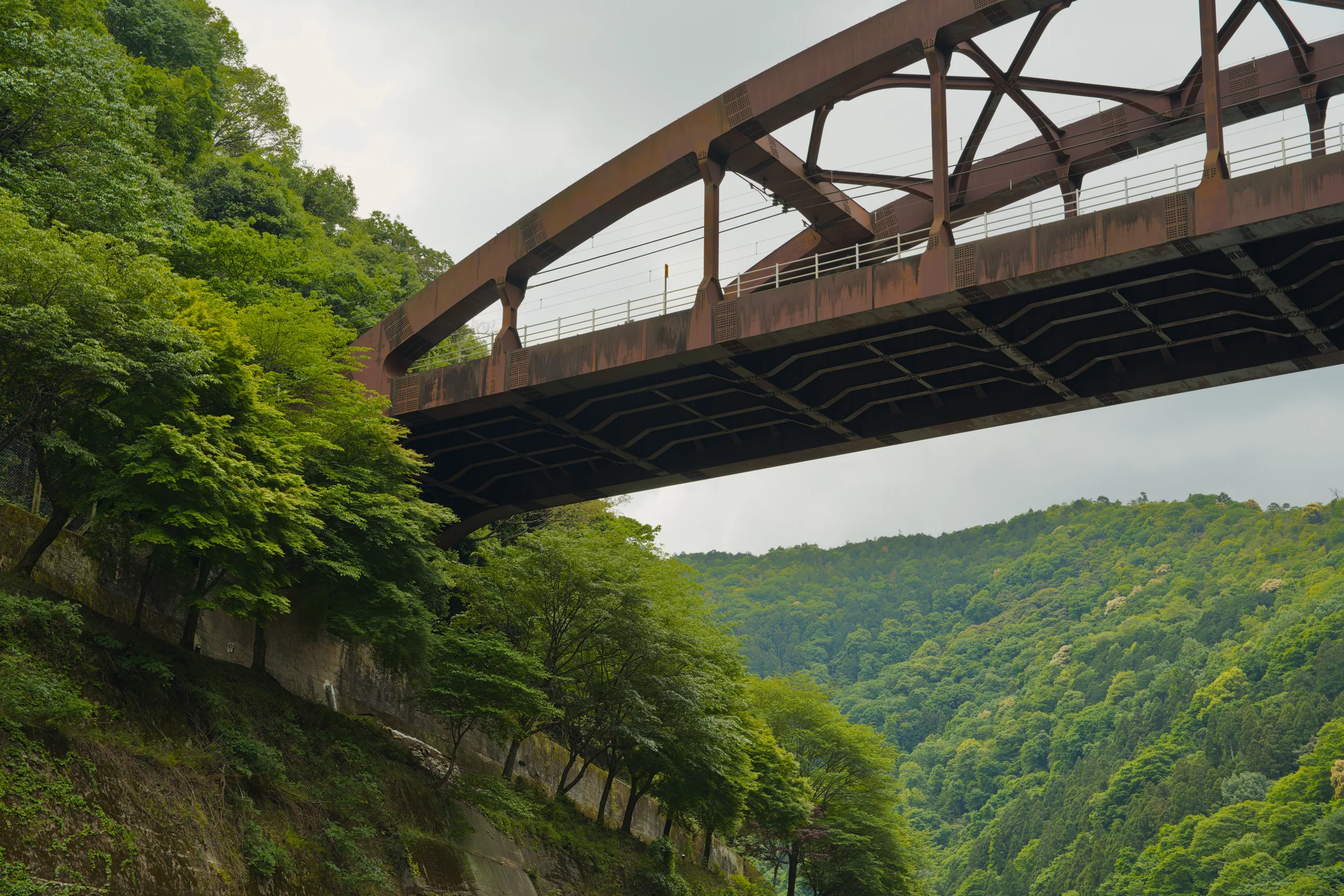 A steel truss bridge arches over a river gorge lined with steep green hills.