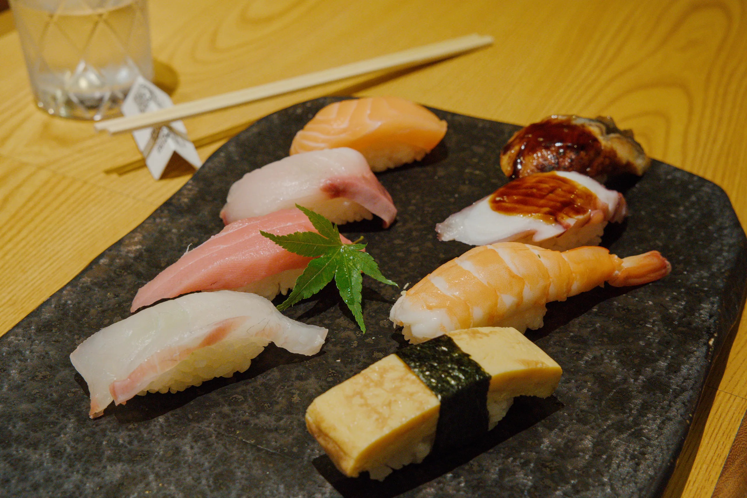 Nigiri sushi arranged on a black stone plate with pickled ginger and wasabi.