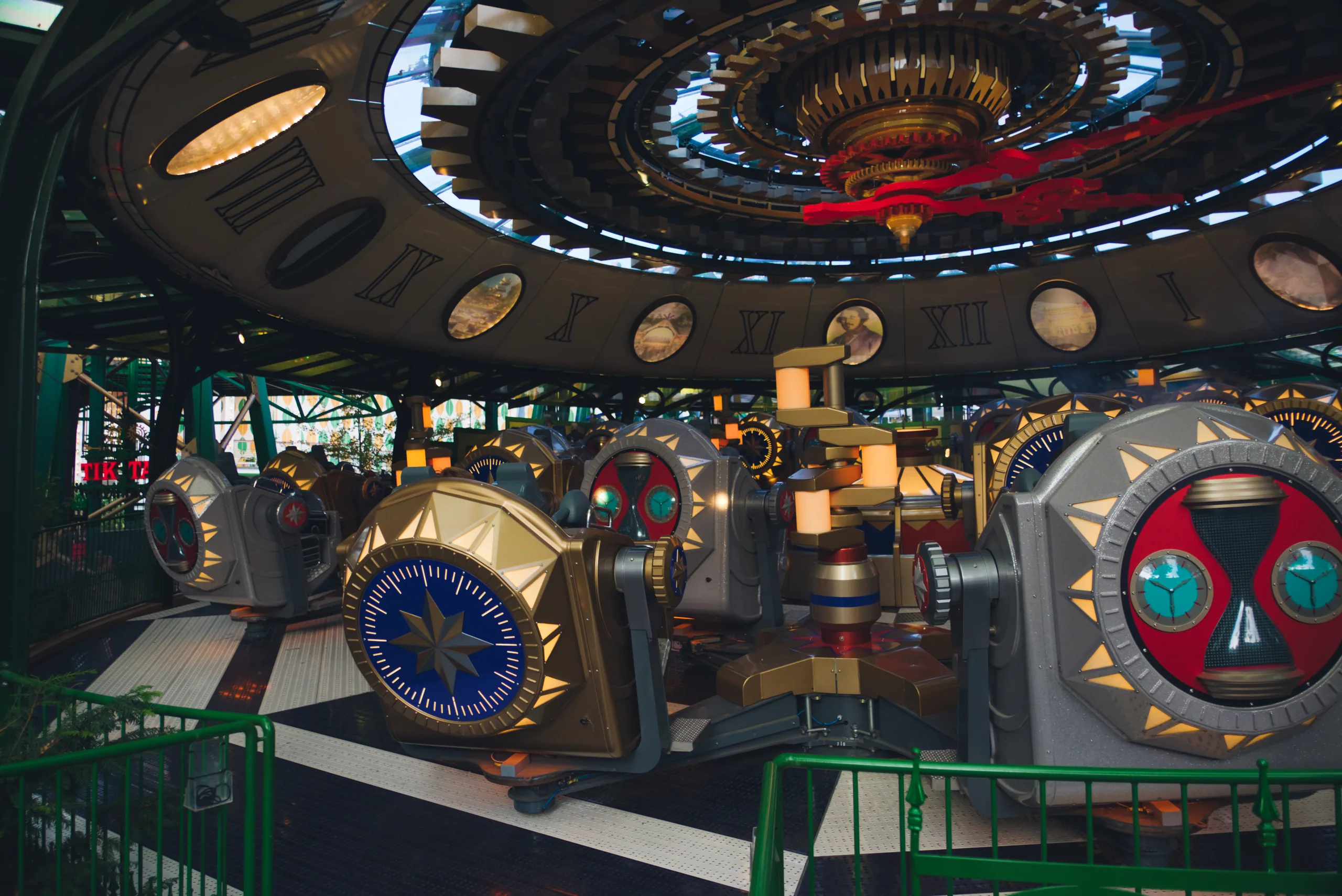 A vintage fairground ride with painted faces and clock dials on its cars, under an ornate illuminated canopy.