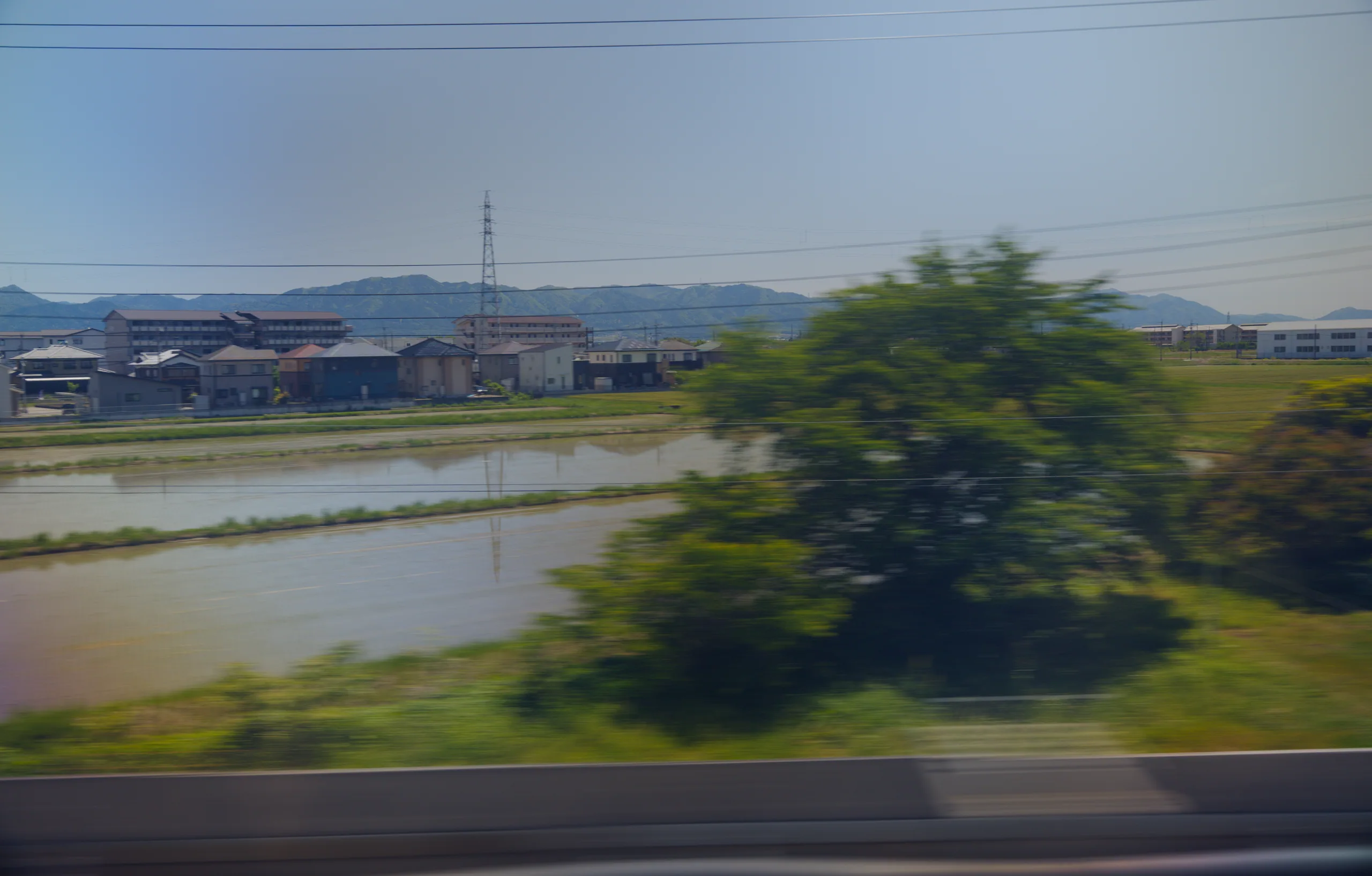Rice paddies and rural fields receding toward mountains, photographed from a moving vehicle.