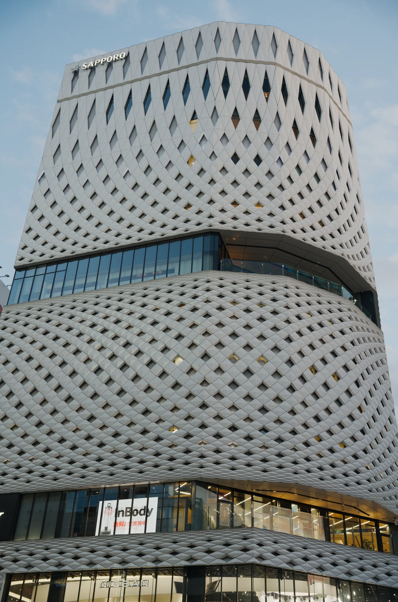 Cylindrical modernist building with a diamond-perforated concrete shell and teal-colored band.