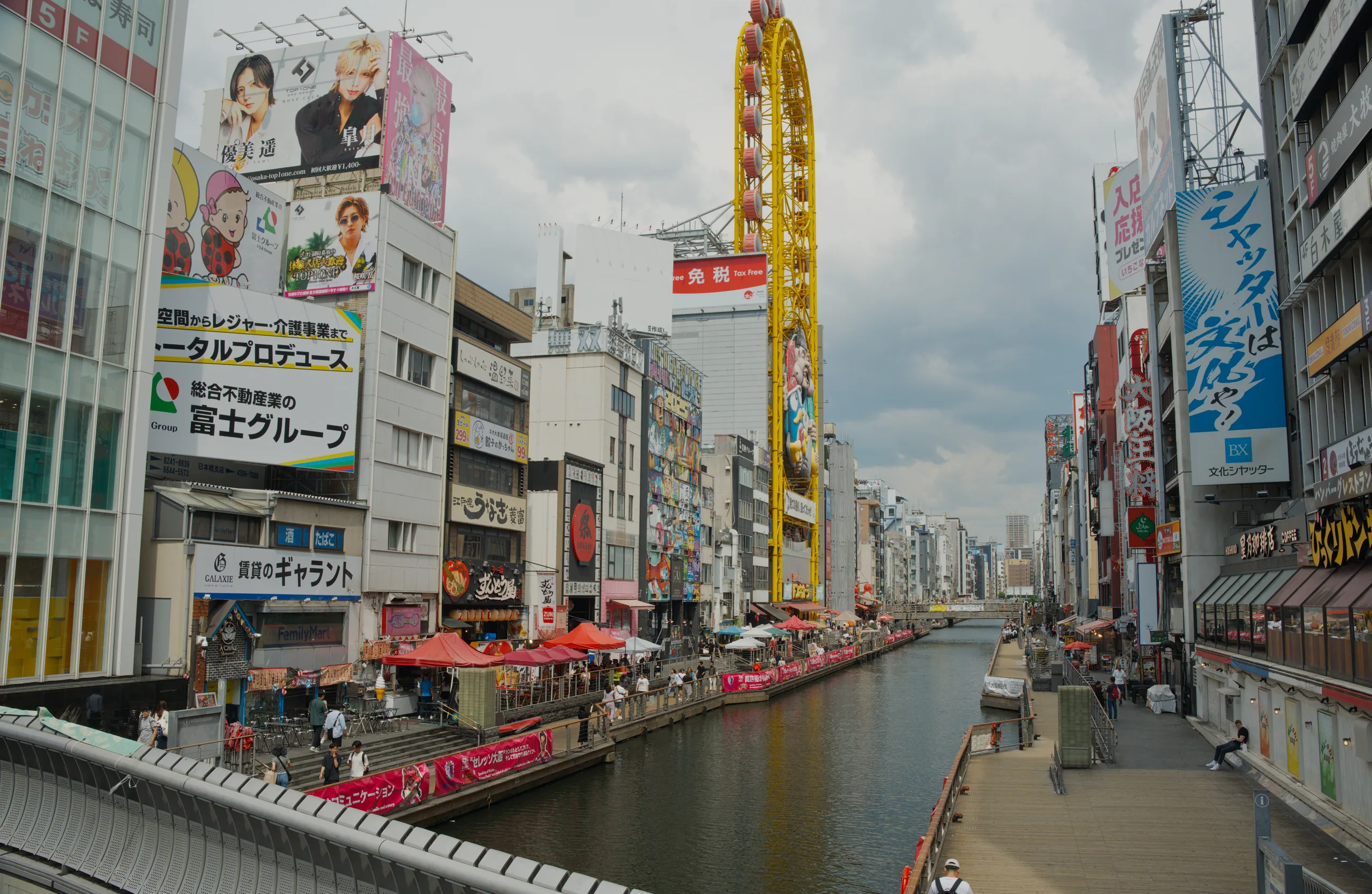 Urban waterfront with commercial buildings, promotional signage, and crowds along the canal.