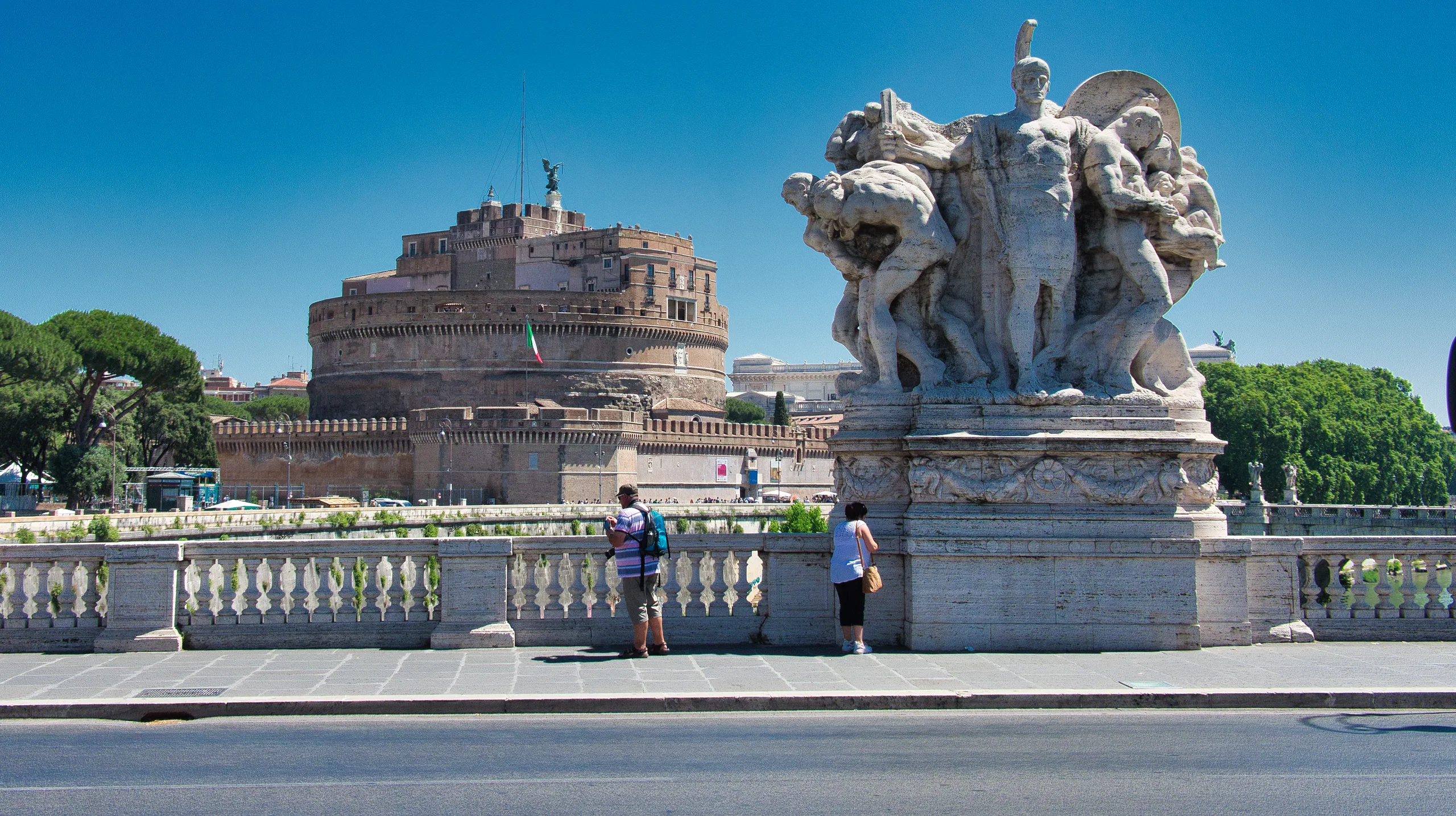 Castel Sant'Angelo across the river with a marble sculptural group on the bridge parapet in the foreground.