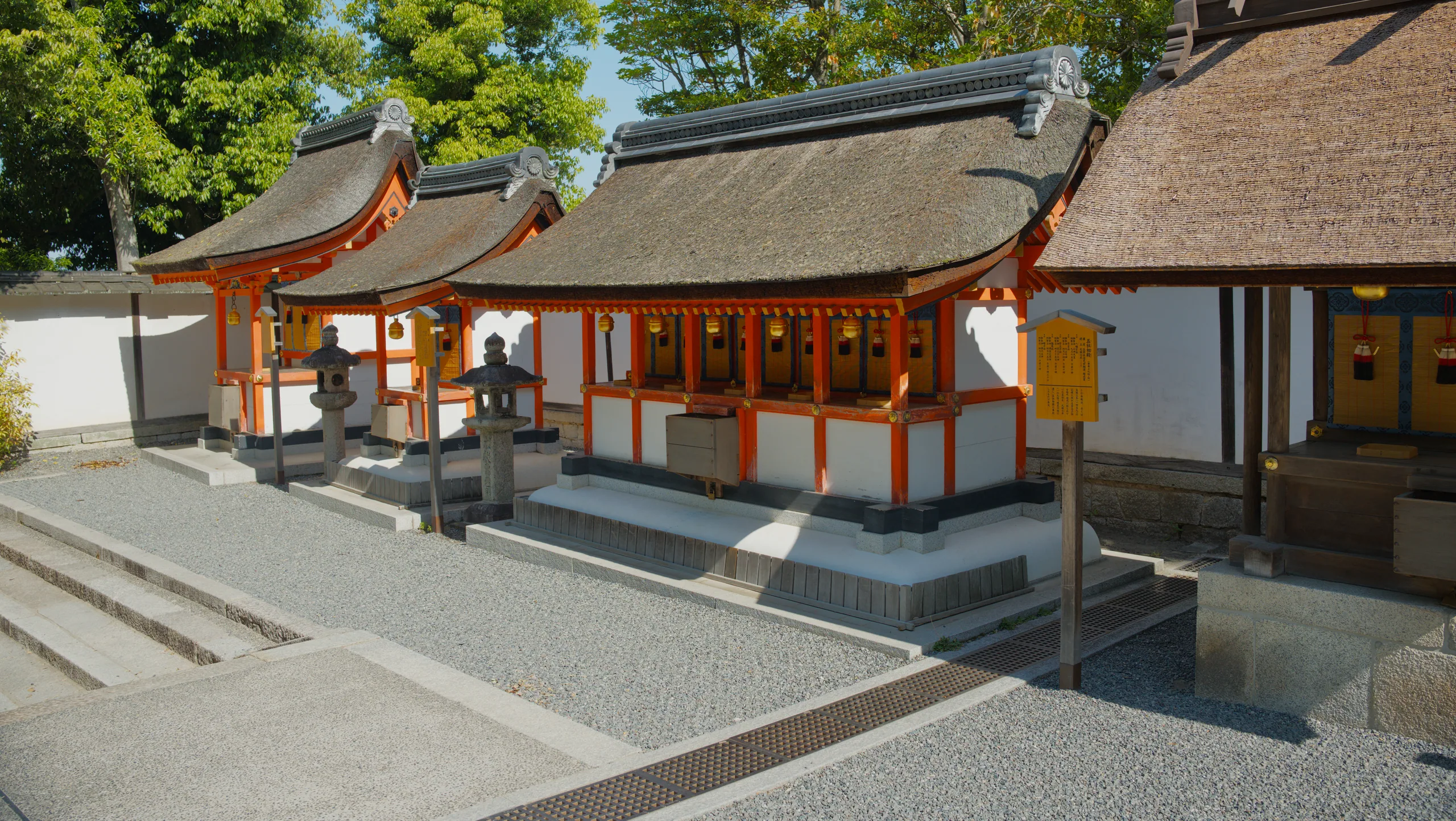 A Japanese shrine building with a curved roof and orange structural details, set in a gravel courtyard.