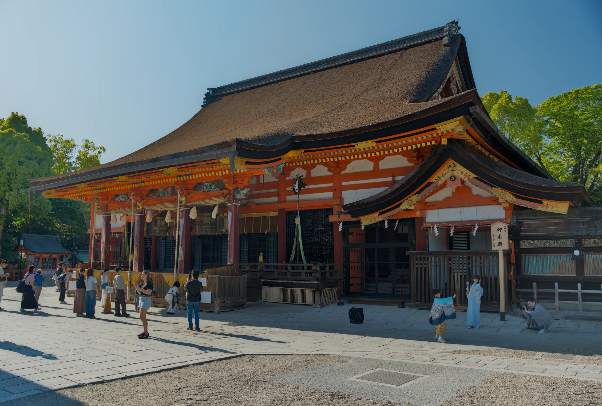 Large red-painted Japanese temple with broad courtyard and visitors on a clear day.