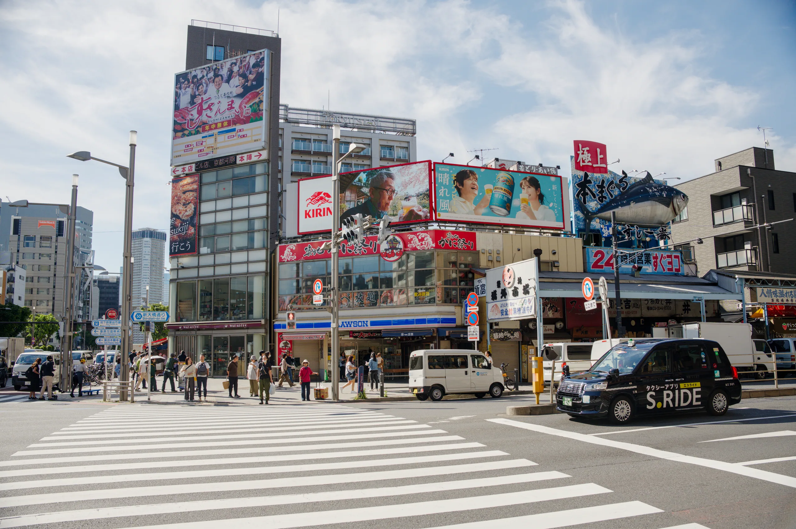A zebra crossing in an urban intersection with tall buildings, Japanese signage, and vehicle traffic.