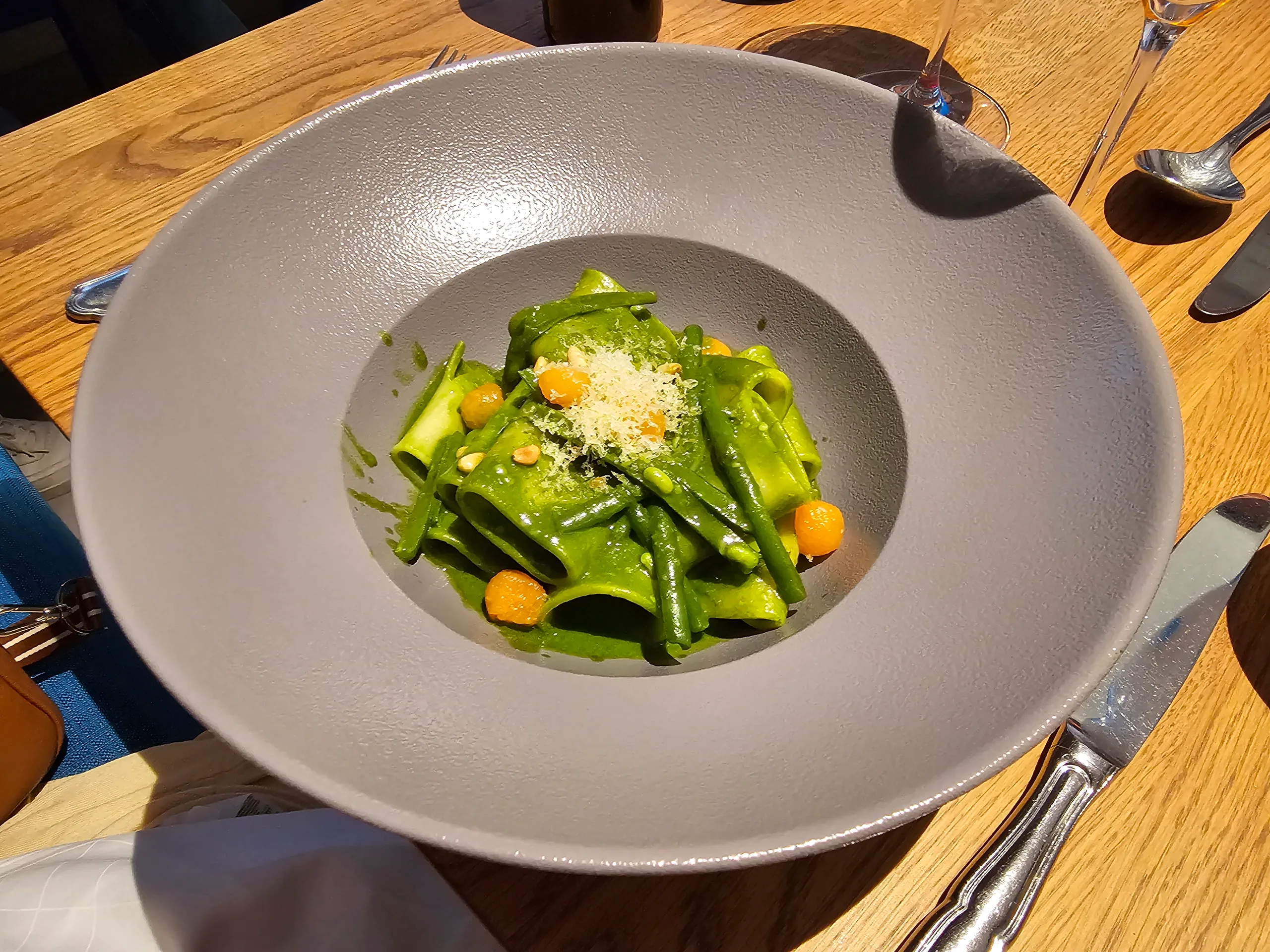 A bowl of green ribbon pasta with beans, grated cheese and dots of orange puree, seen from above.