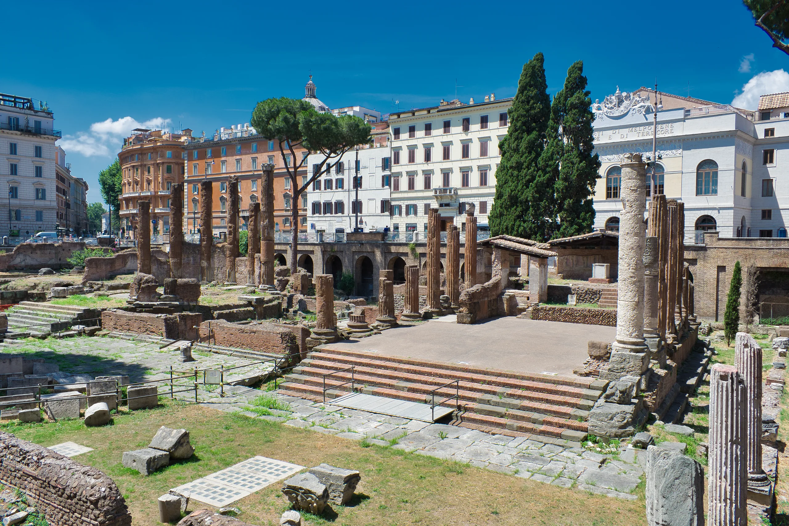 The excavated temple ruins of Largo di Torre Argentina in Rome, broken columns and stone platforms below modern street level.
