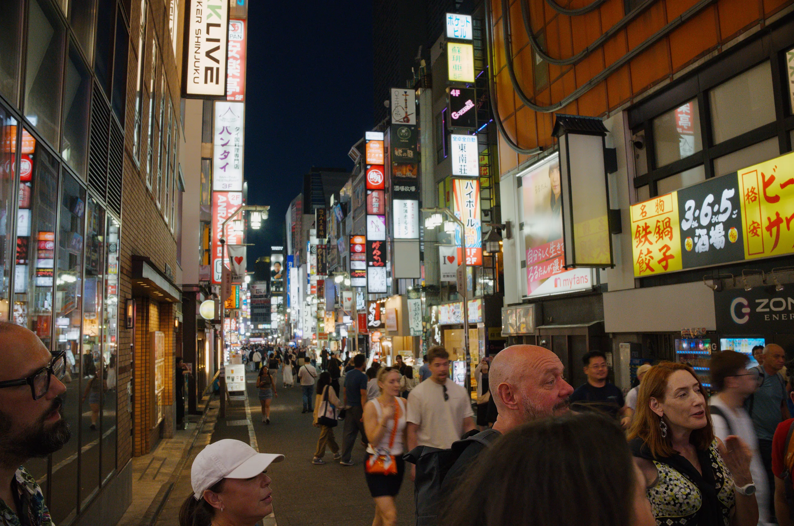 A narrow Tokyo street at night packed with people, both sides stacked with glowing vertical signs in Japanese receding into the distance.