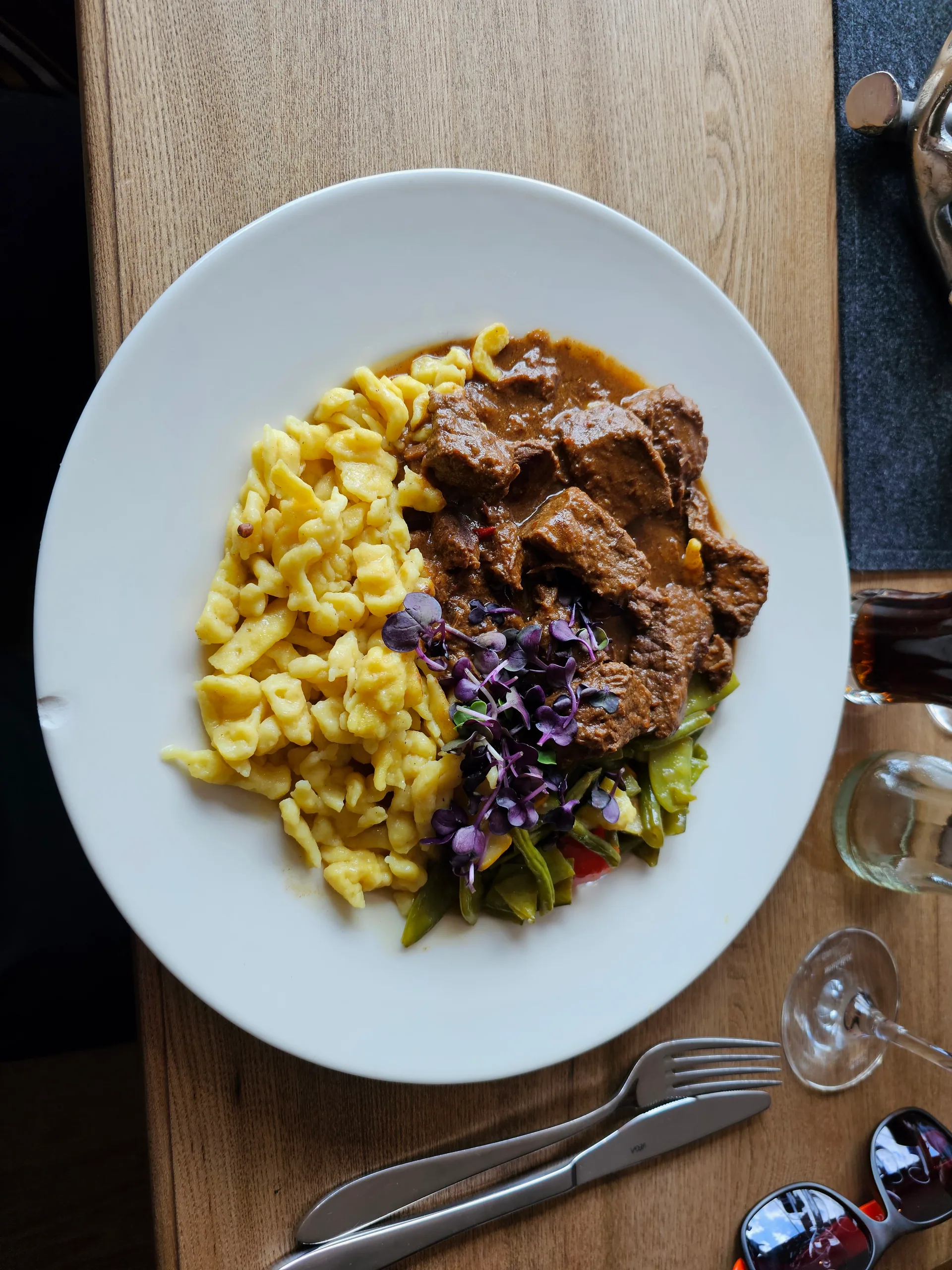 Goulash with spaetzle and a small salad on a white plate, seen from above on a wooden table.