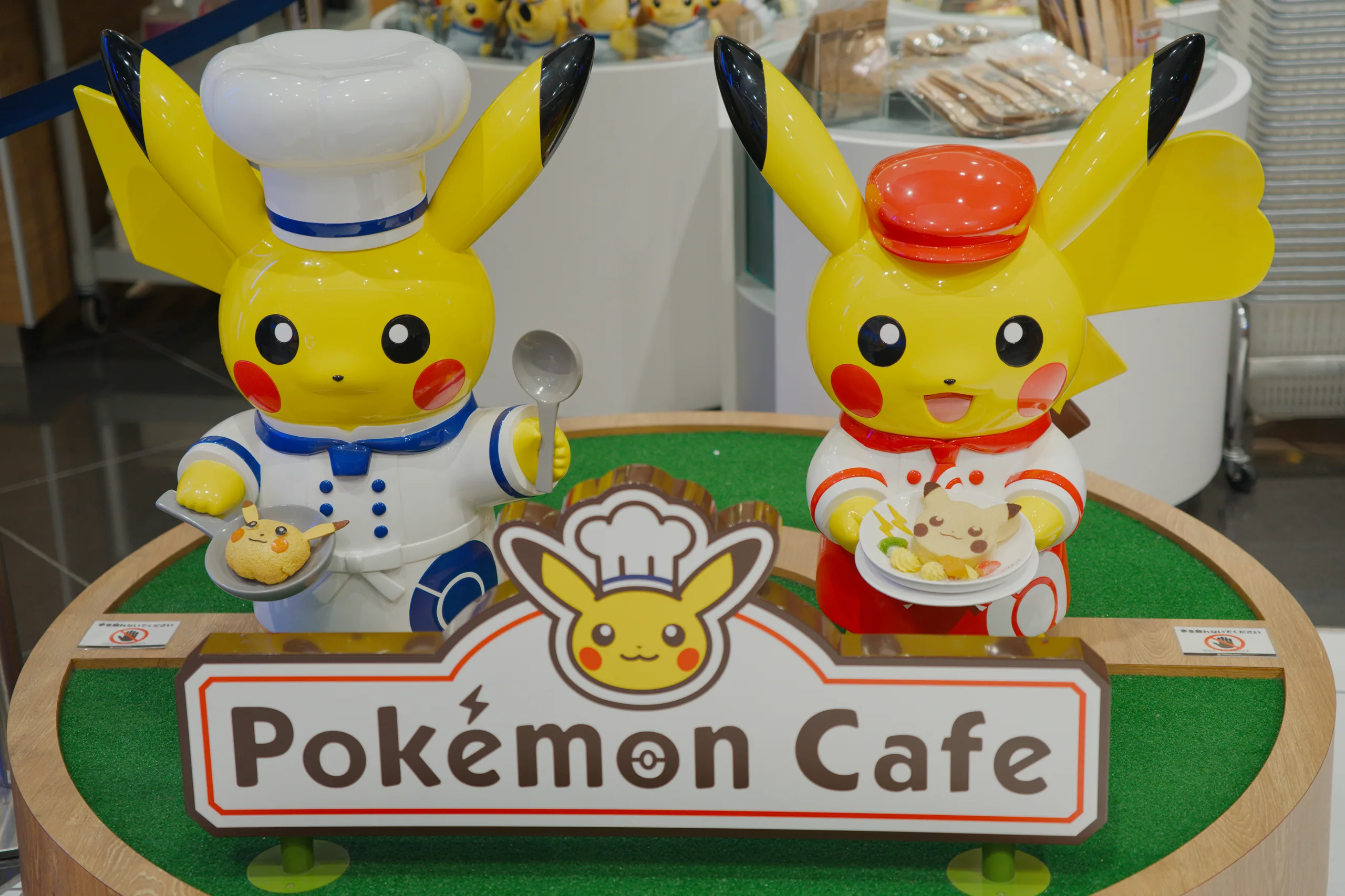 Pokémon Cafe storefront signage with large Pikachu character sculptures holding food items.