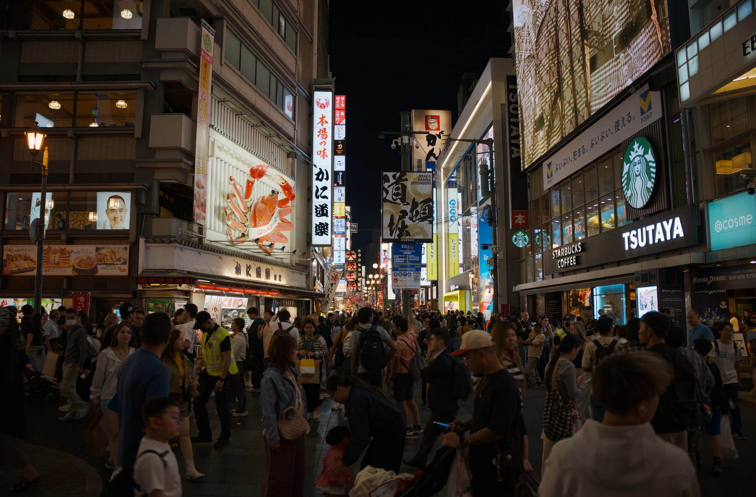 Crowded covered pedestrian shopping street at night with shopfronts and illuminated storefronts.