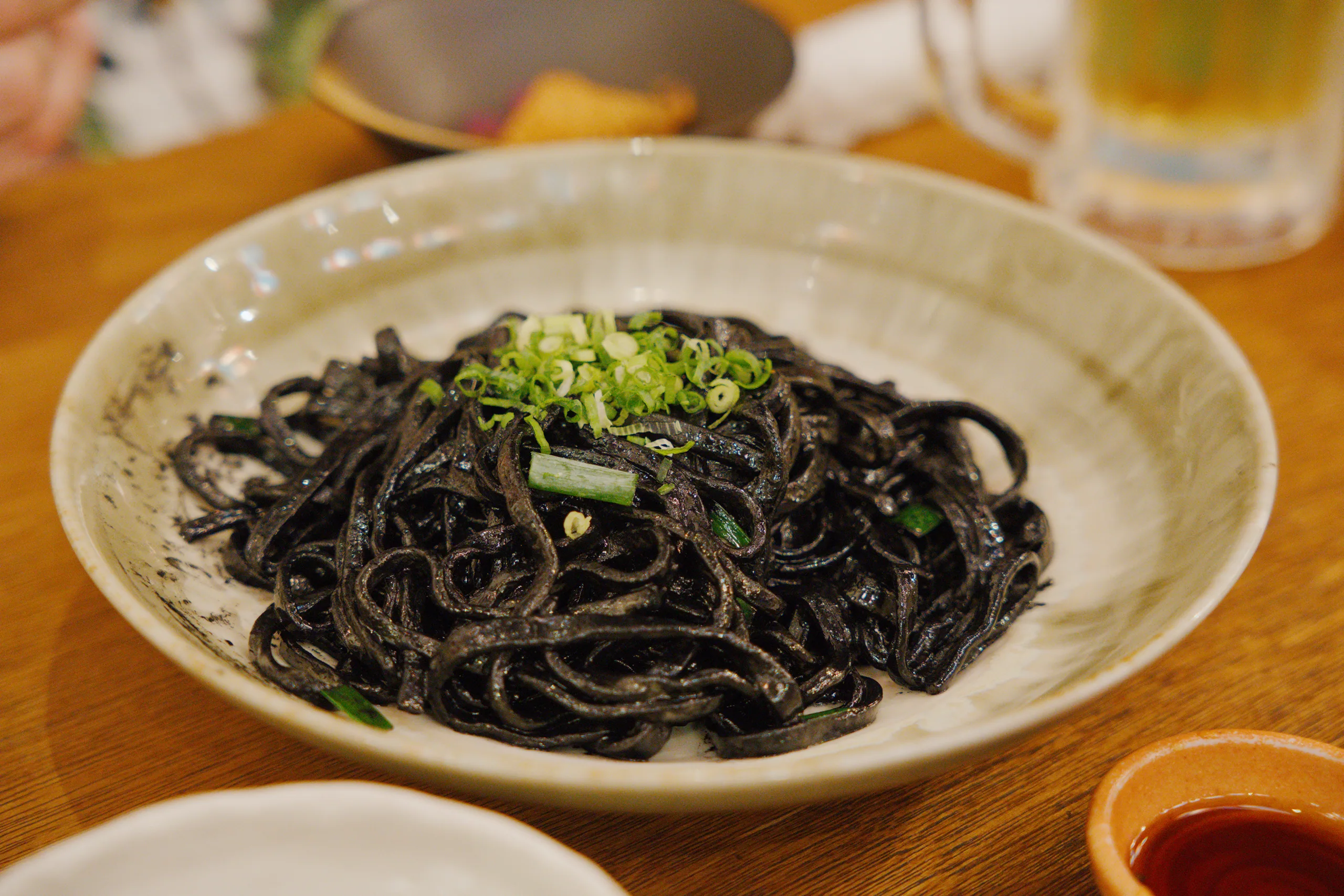 Plate of dark noodles garnished with bright green microgreens on a wooden table.