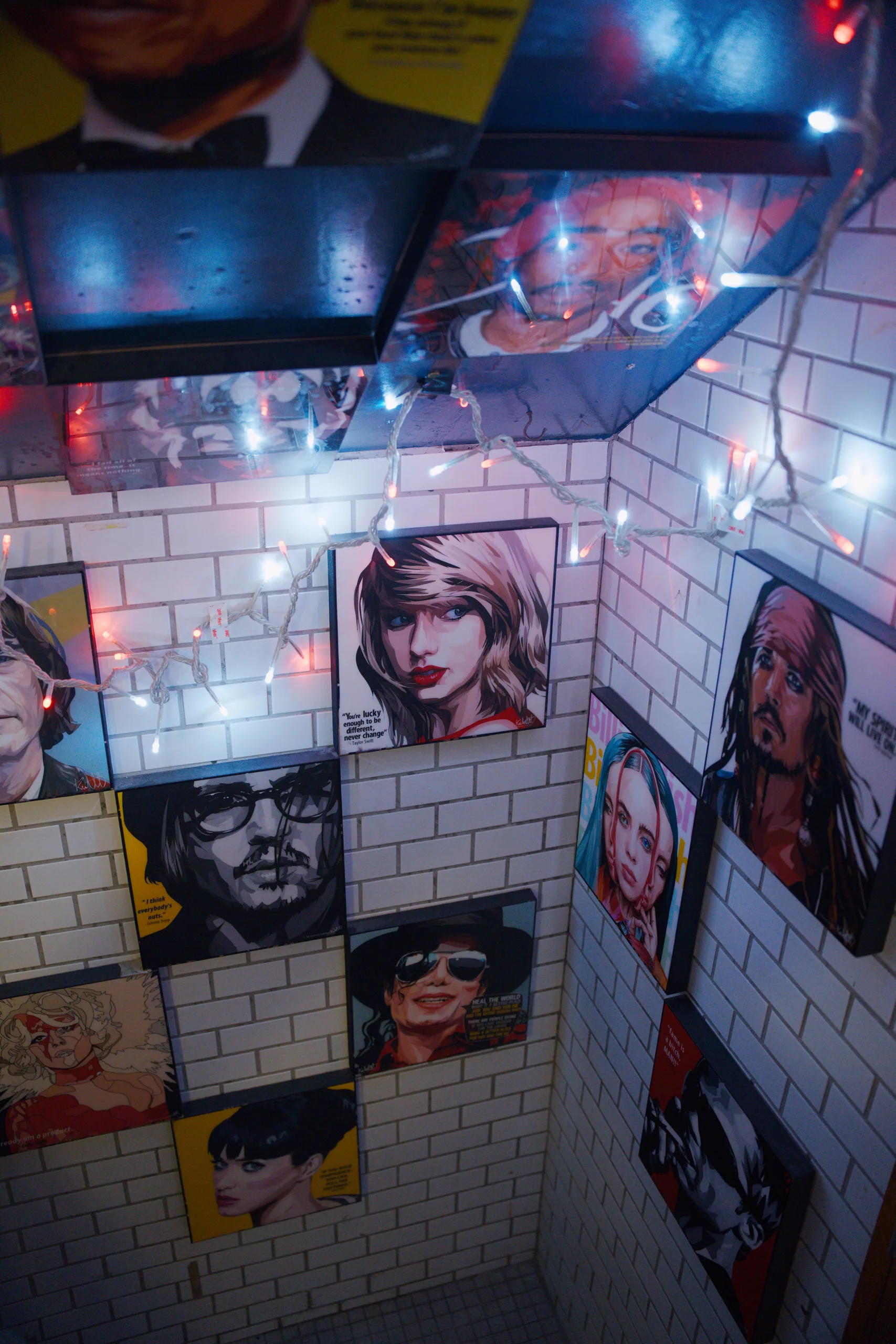 Illuminated portrait photographs mounted on a white brick wall in a dimly lit venue with neon signage.