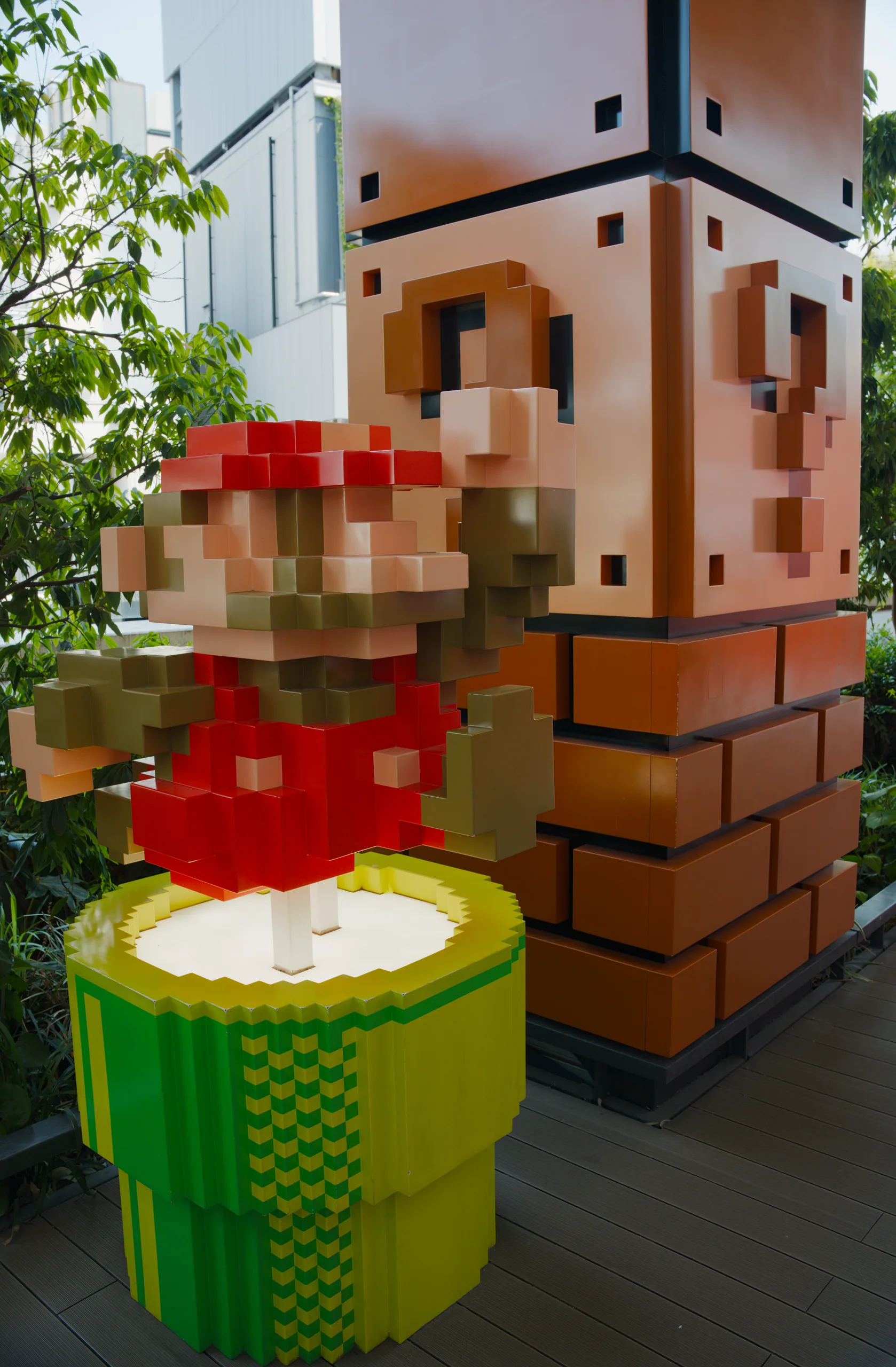 Large pixelated creature figure in red and white atop a green cylindrical base, displayed indoors with brick architecture.