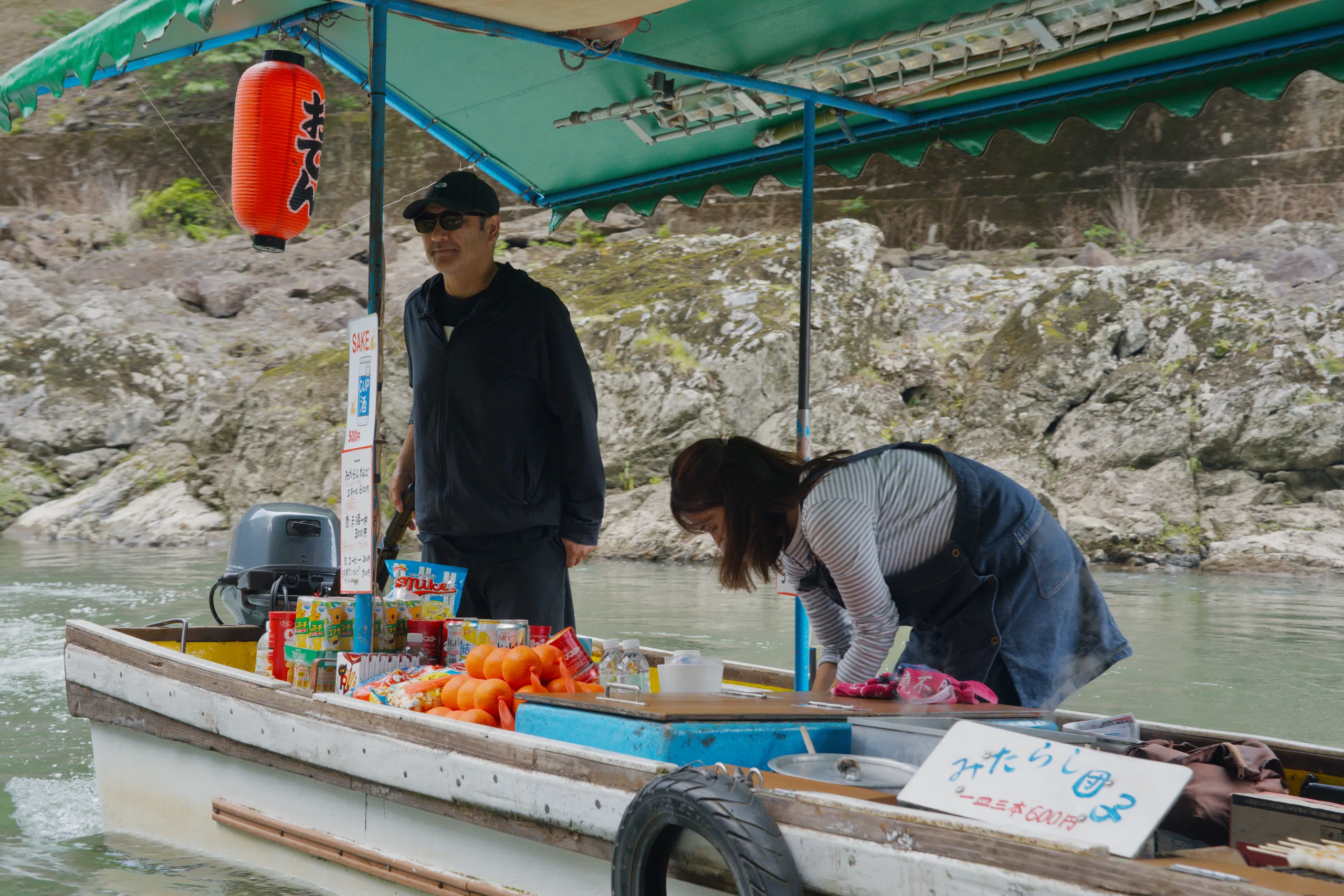 A person works among supplies on a moored boat, with additional boats visible nearby.