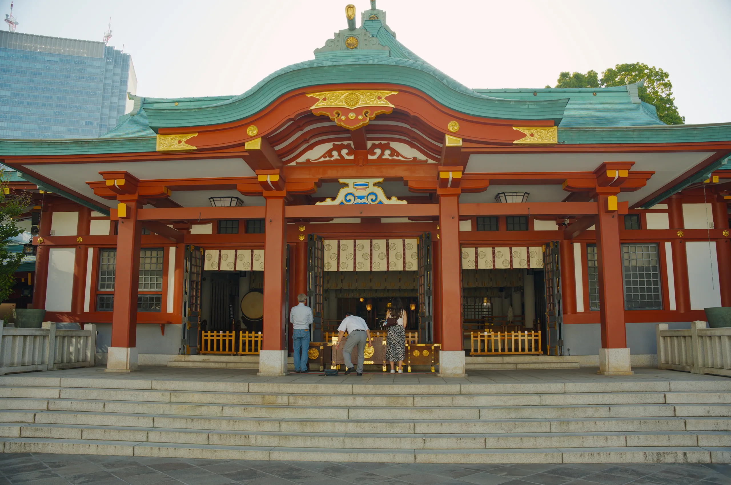 A red temple building with a sweeping curved roof topped in green metal.