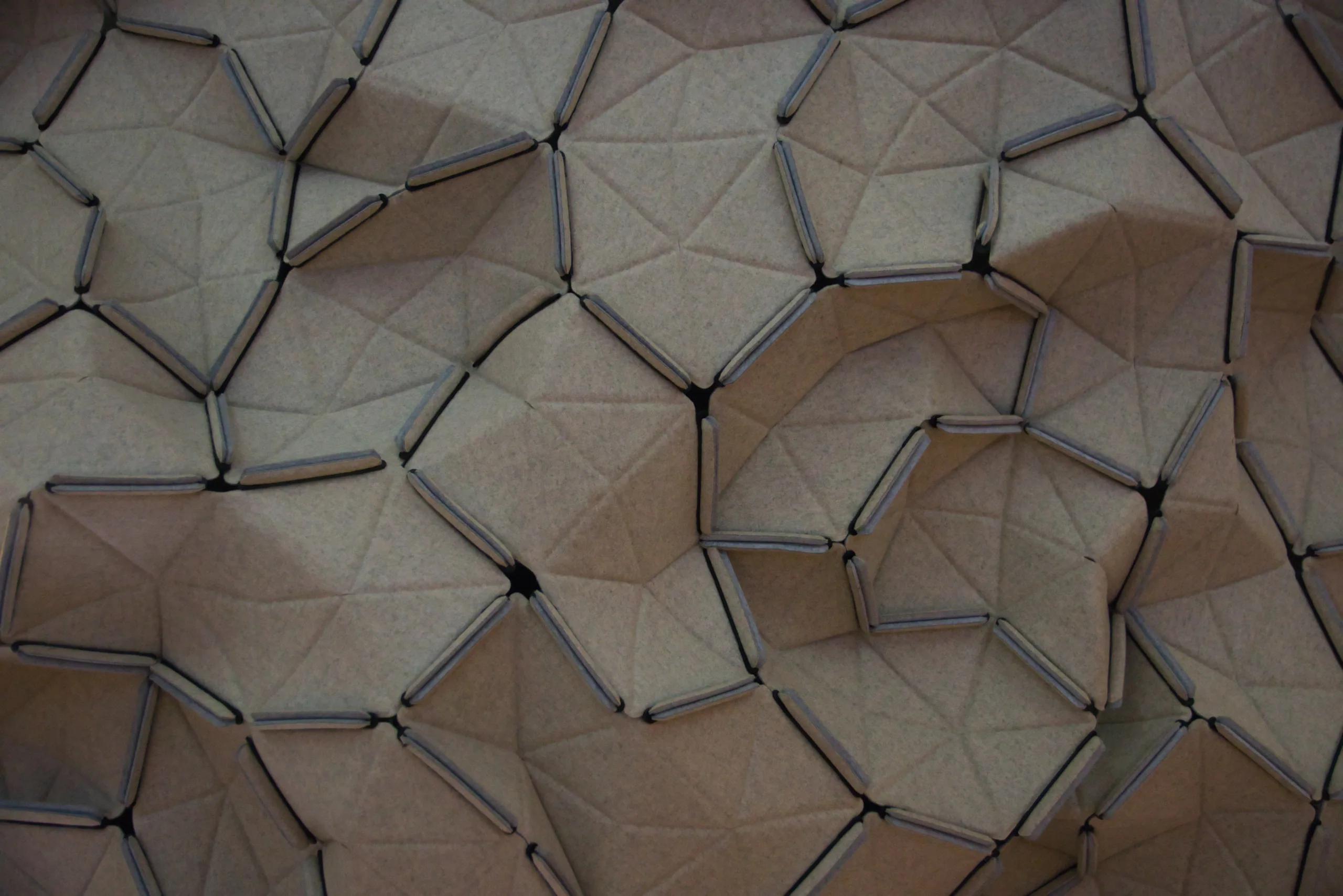 A close view of a folded paper or textile structure of small triangular facets stitched together into an irregular honeycomb.