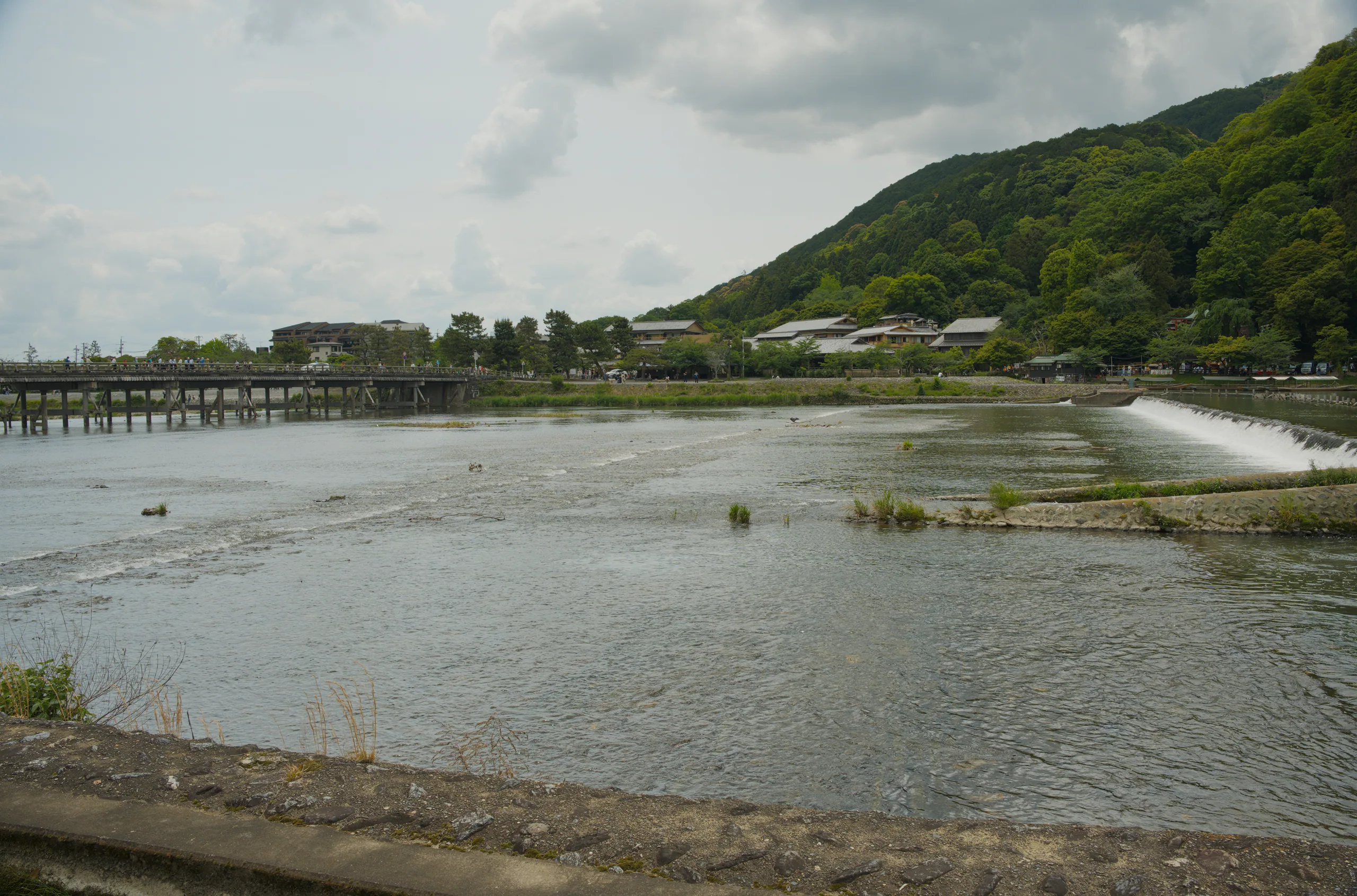 A river valley runs between steep green mountains with a wooden structure on the near shore.