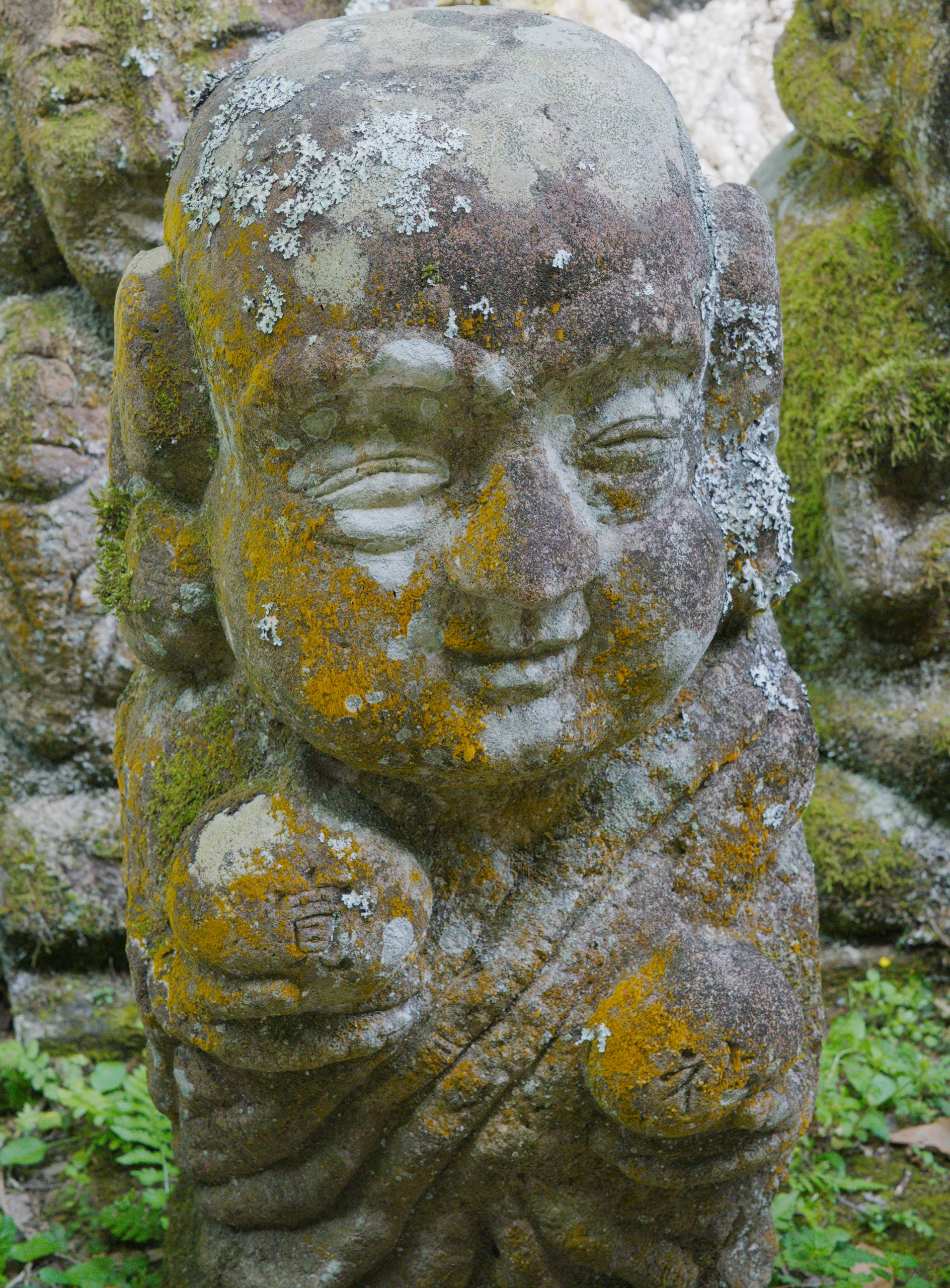 A large carved stone head weathered gray with moss, its face serene, other figures visible in the background.