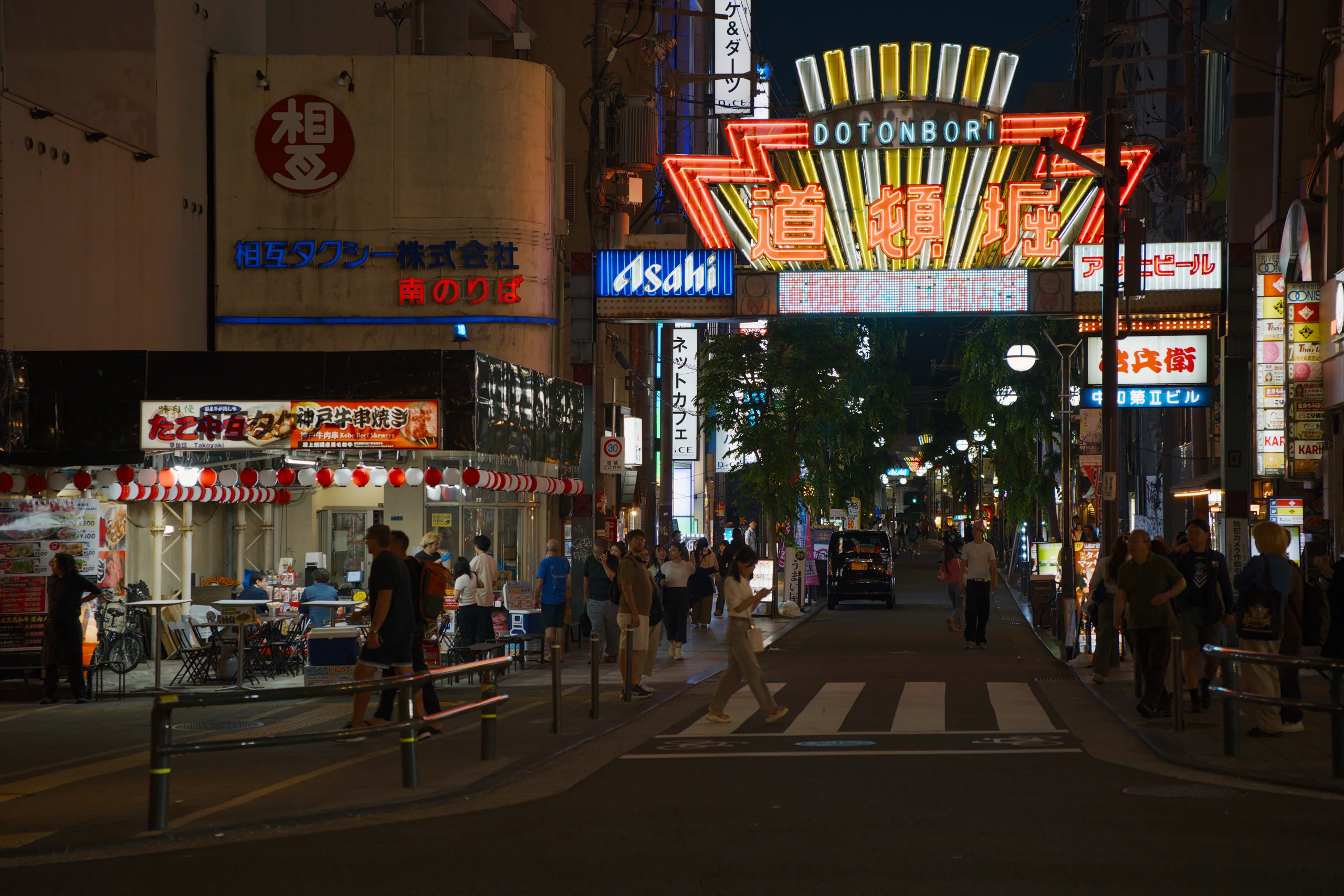 Wide nighttime street crowded with pedestrians beneath bright neon advertisements and tall buildings.