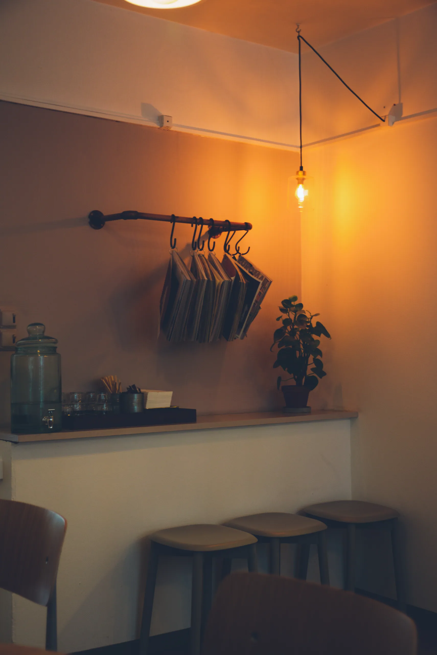 A warmly lit cafe corner with a bare bulb hanging over a counter, menus clipped to a rail on the wall and low stools pulled up.