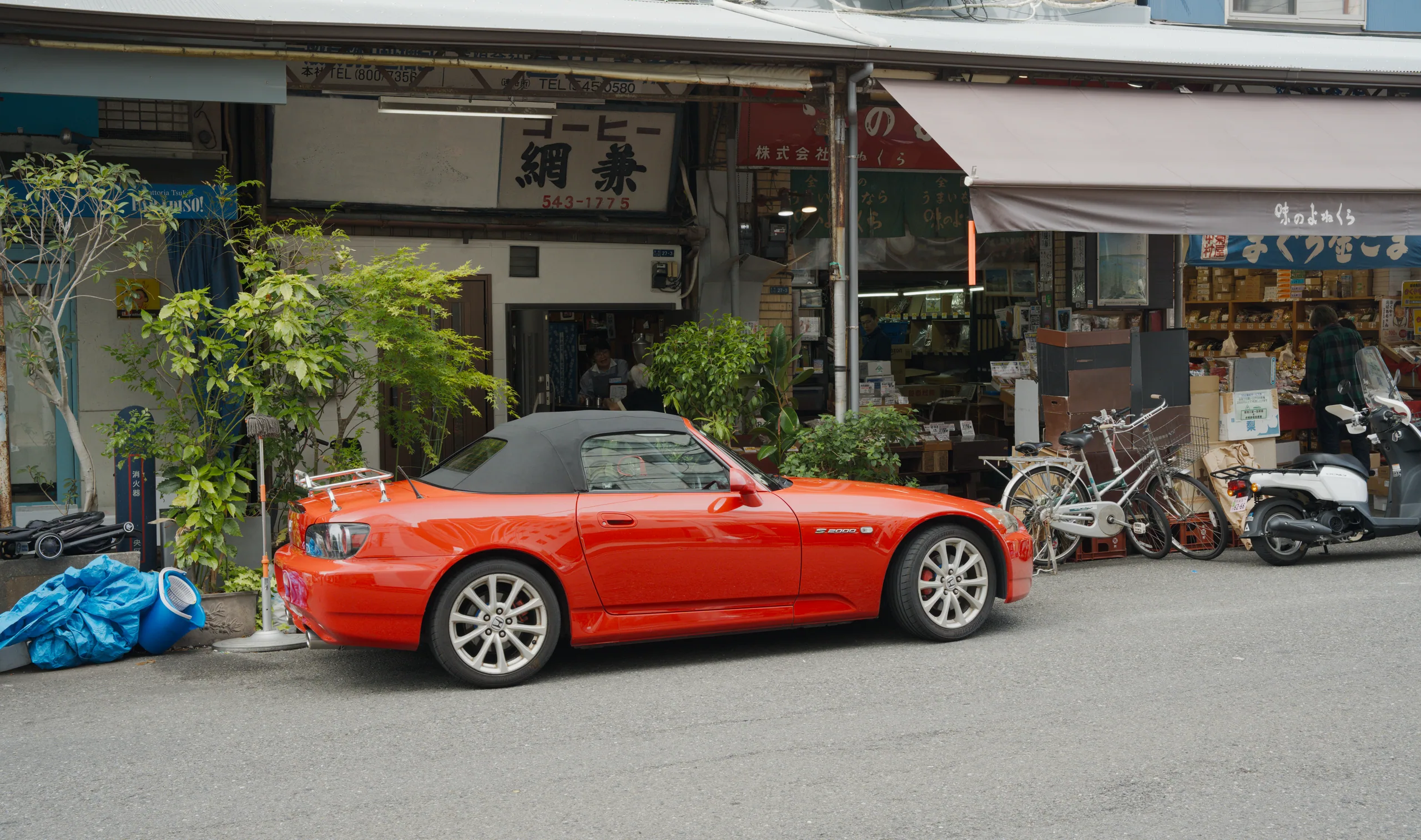 A red convertible parked on a Japanese street with storefronts and signage.