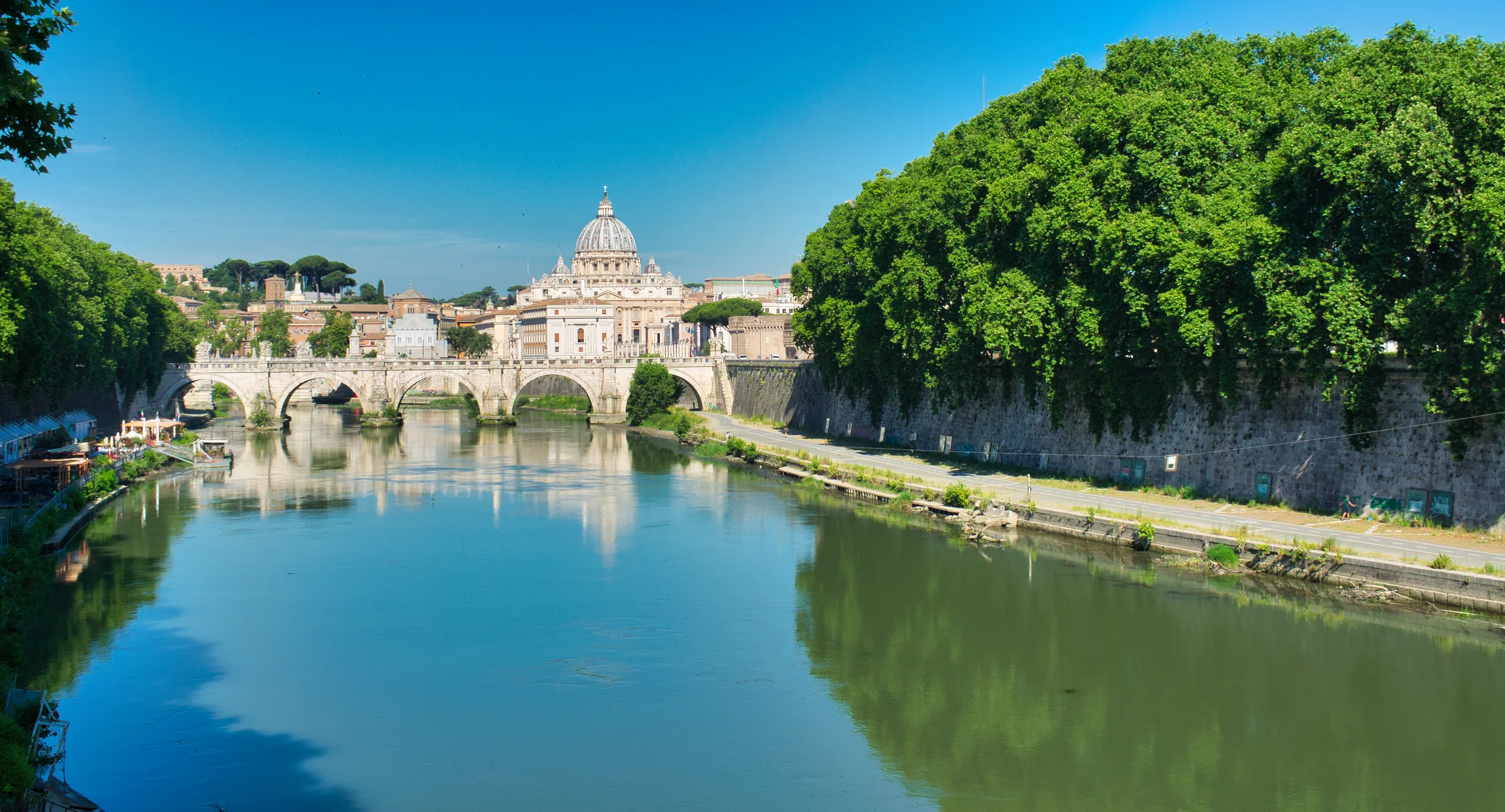 The Tiber curving between tree-lined embankments, a bridge crossing it and St Peter's dome on the skyline.