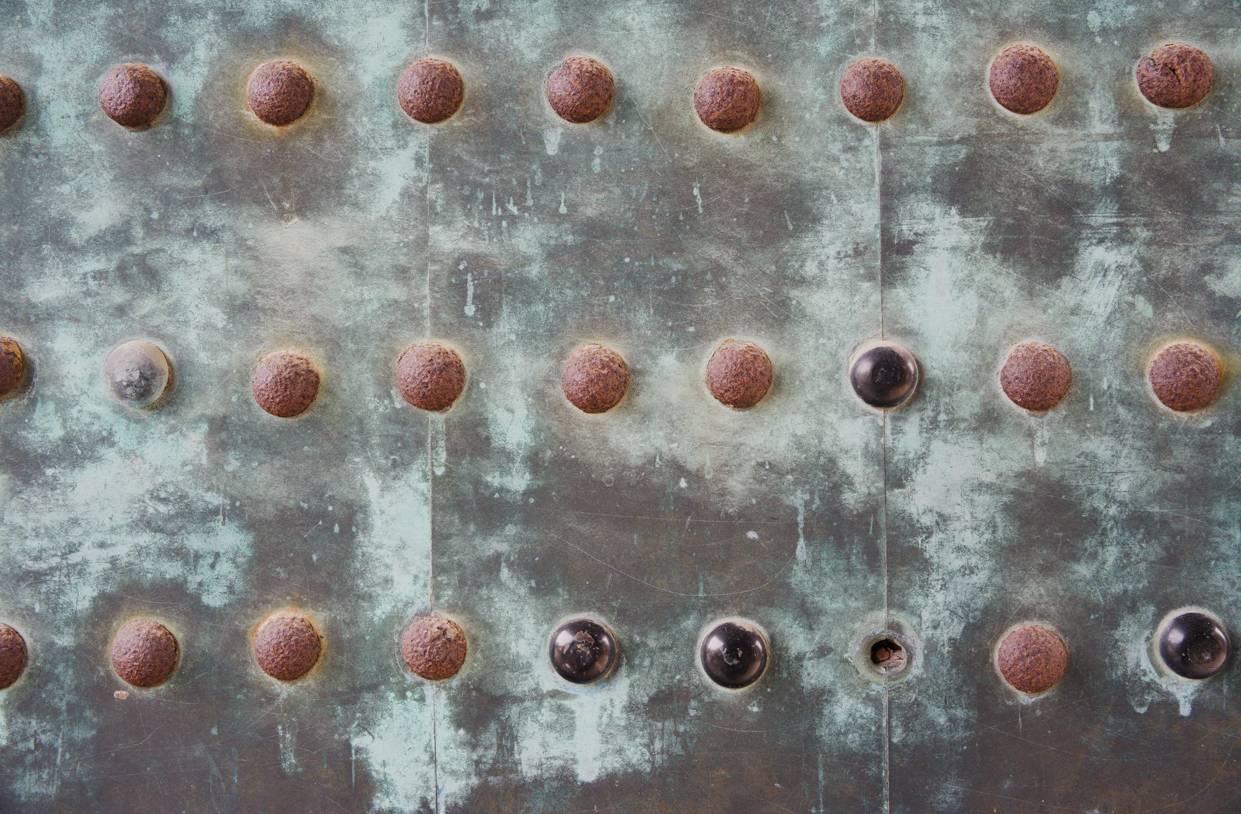 Weathered metal wall surface with a regular grid of circular studs showing rust and discoloration.