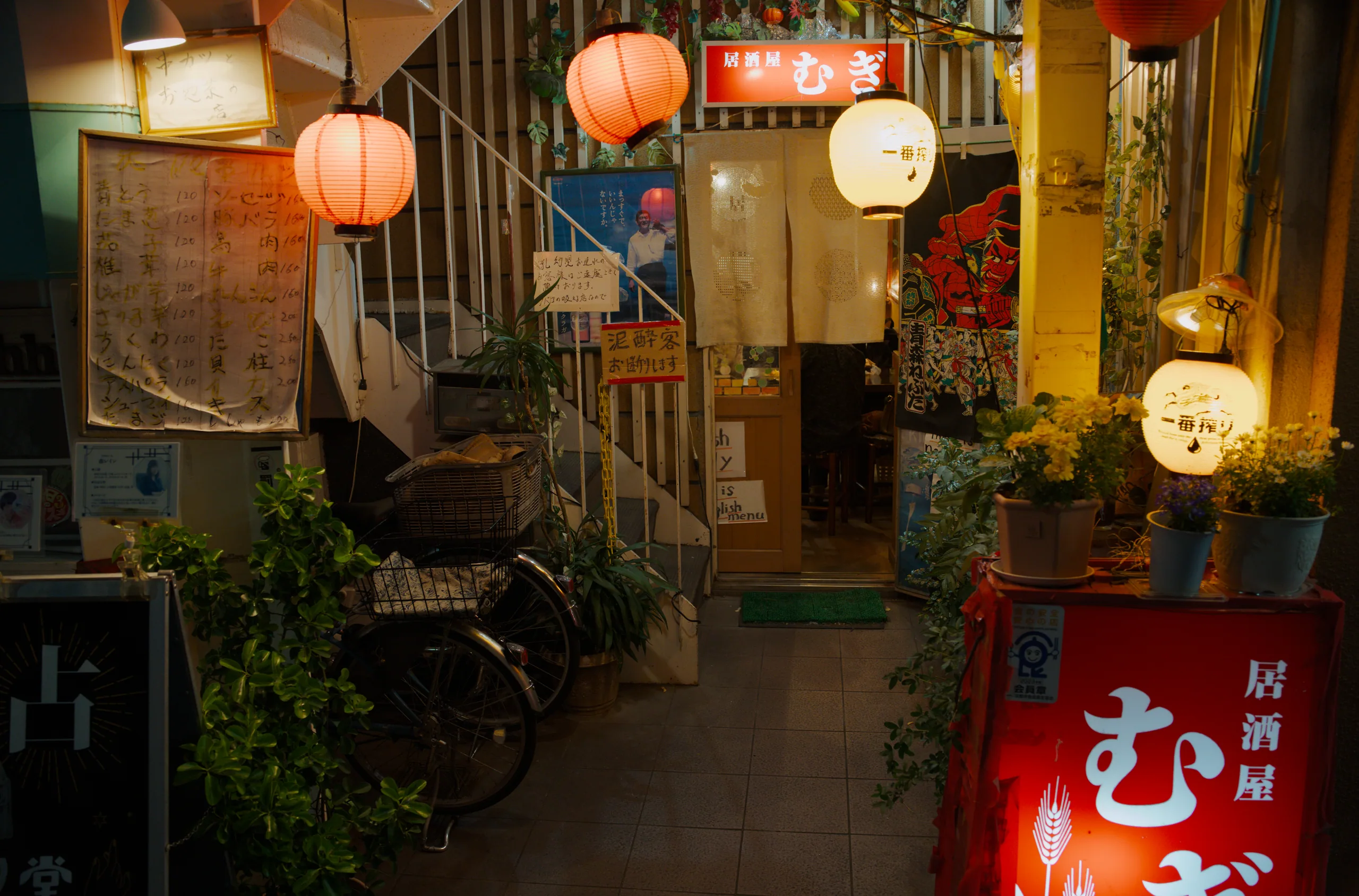 Alley entrance decorated with hanging paper lanterns, wooden storefronts, and shop signs.