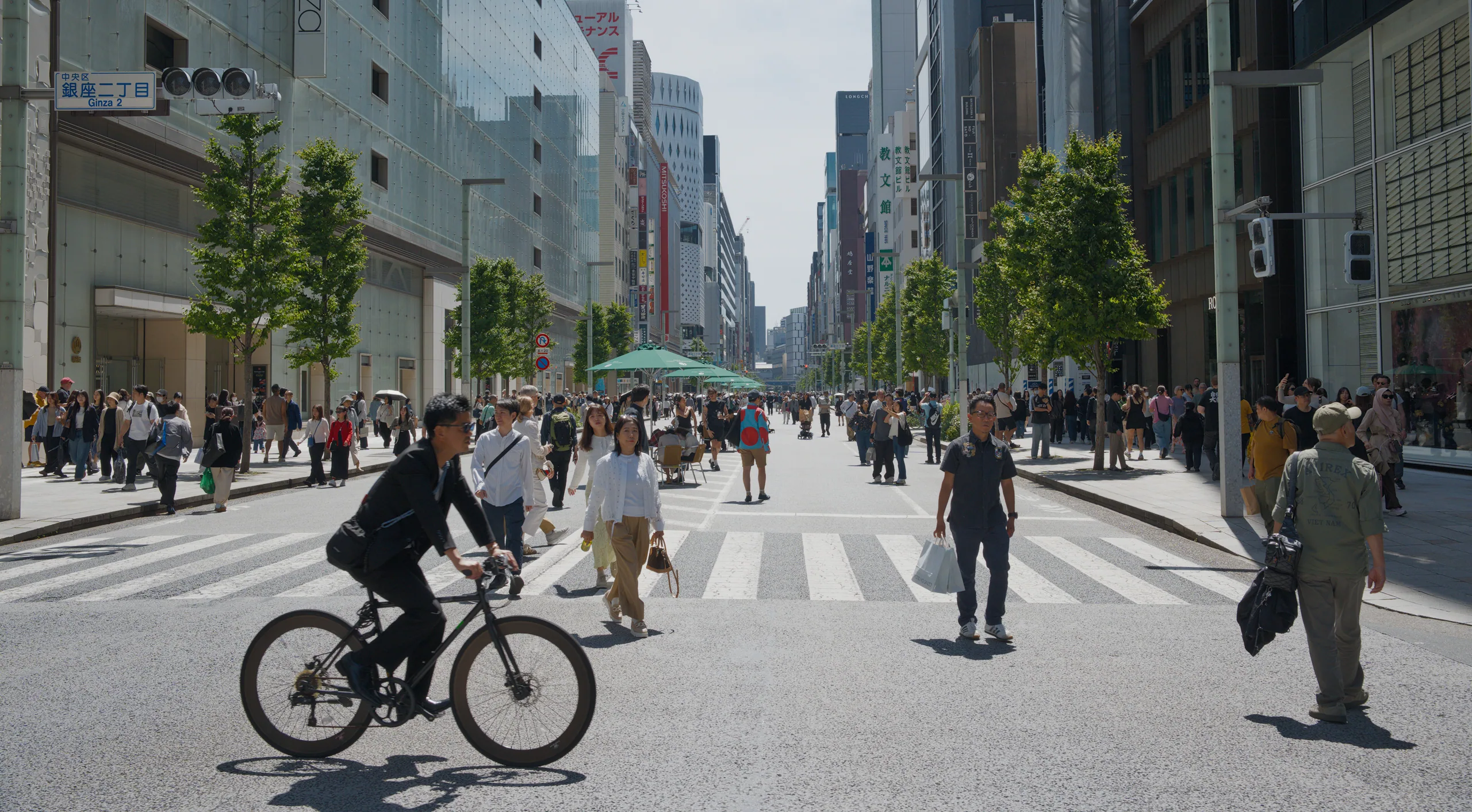 Cyclist riding through a crowded pedestrian street lined with tall buildings.