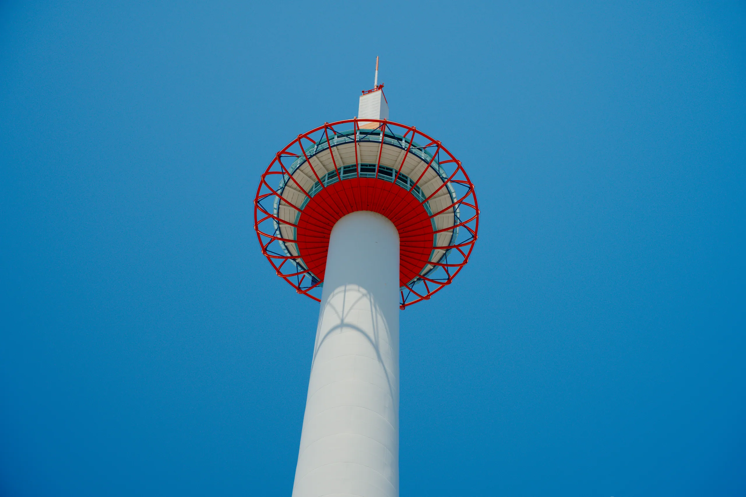 A white tower with a red rotating mechanism at the crown, photographed from below against a clear sky.
