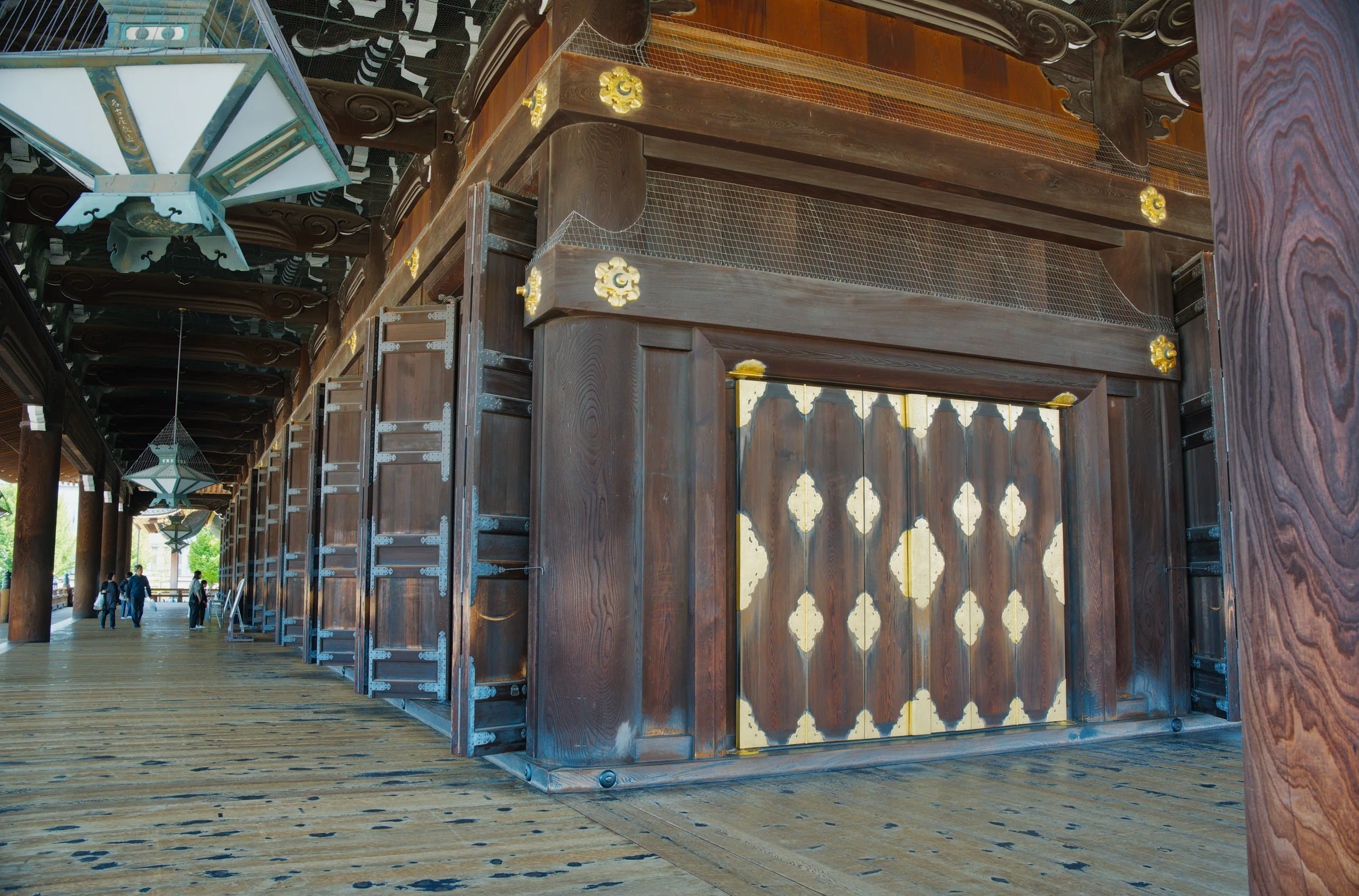A covered wooden colonnade with hanging lanterns and traditional shop fronts along a temple corridor.