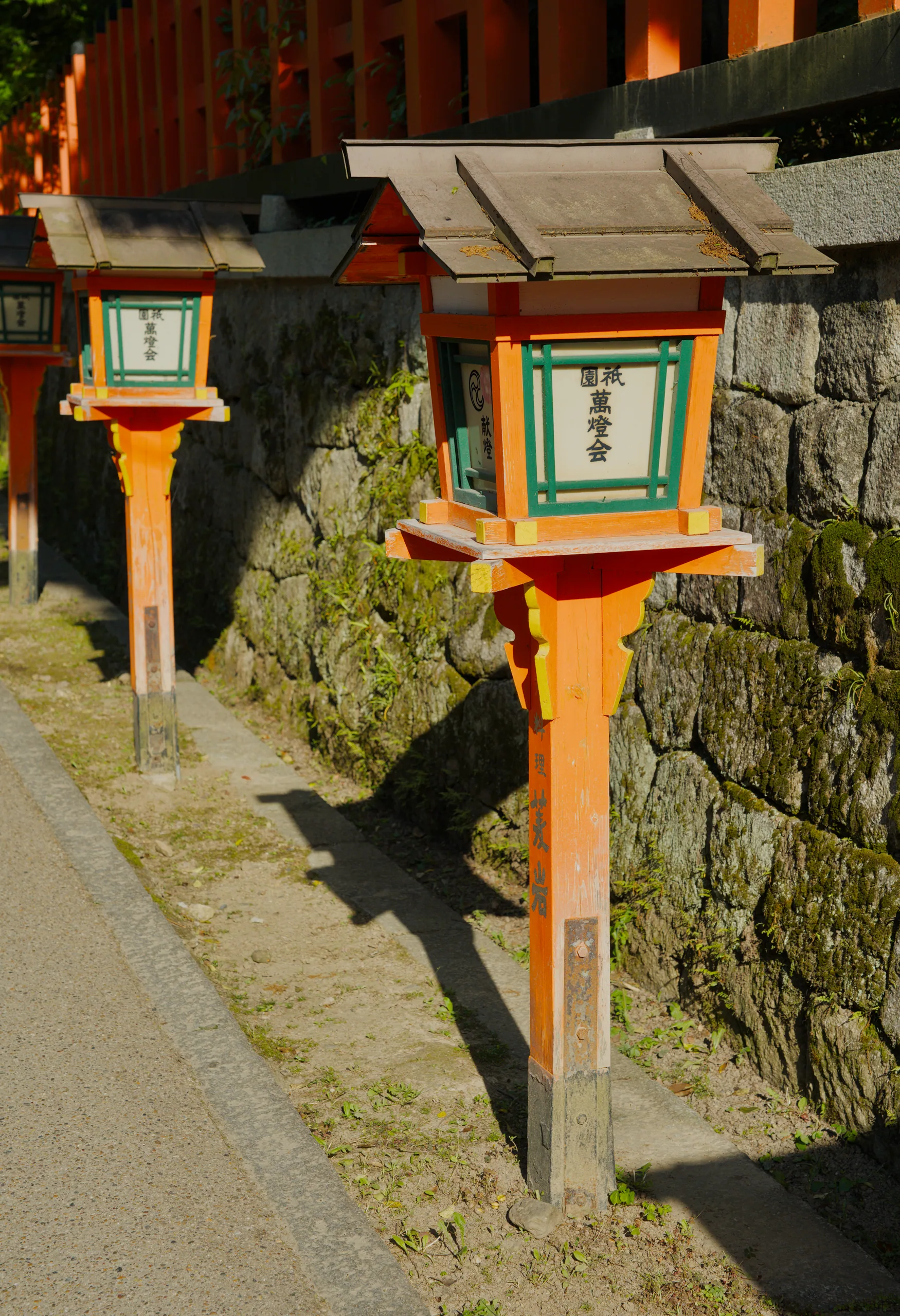 Yellow and orange wooden shrine post with a green ornamental box on top beside a stone wall.