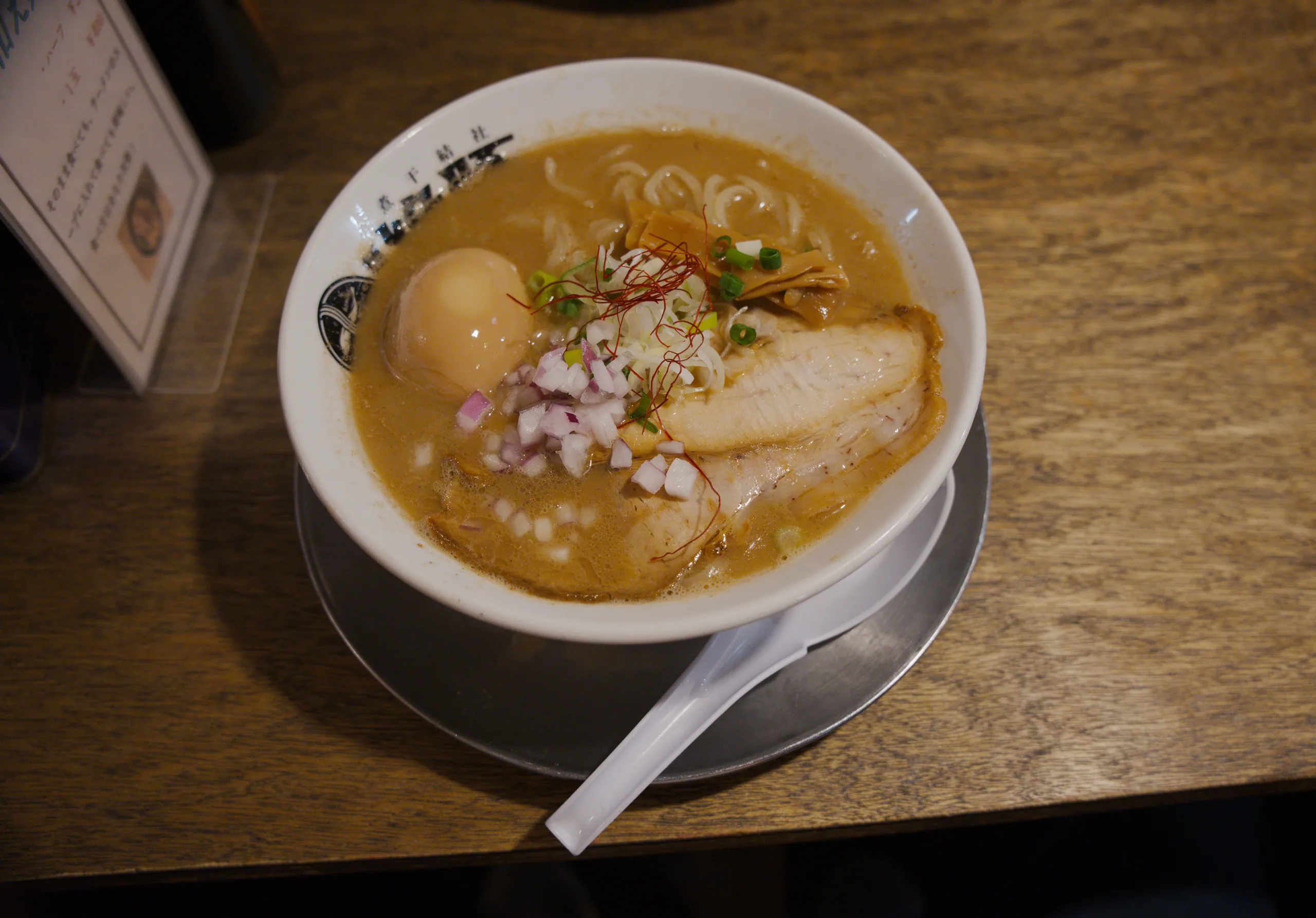 Ramen with golden broth, sliced pork, soft-boiled egg, and pickled pink ginger in a white bowl.