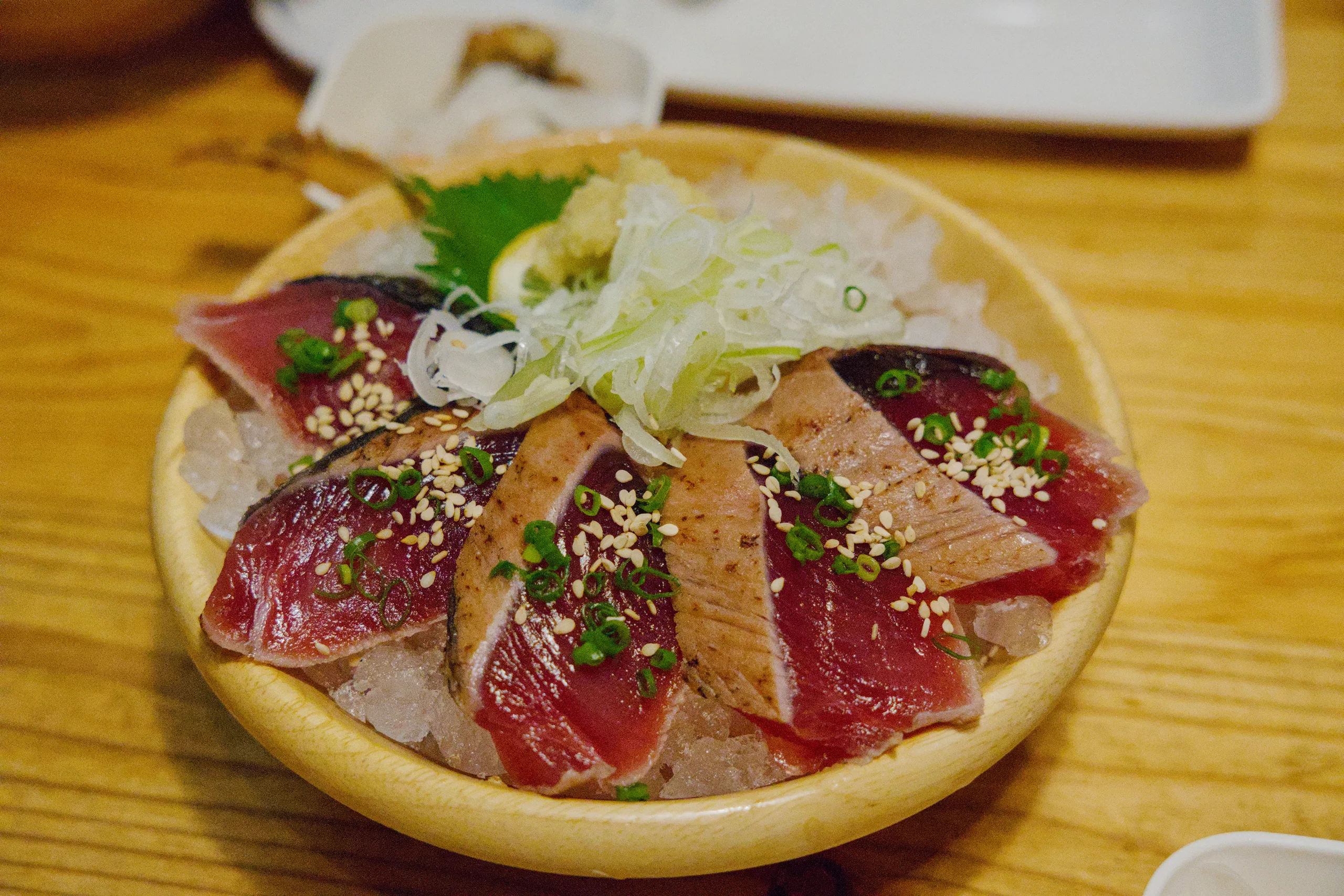 Sliced raw beef or carpaccio topped with white sesame seeds and fresh green herbs on a white plate.