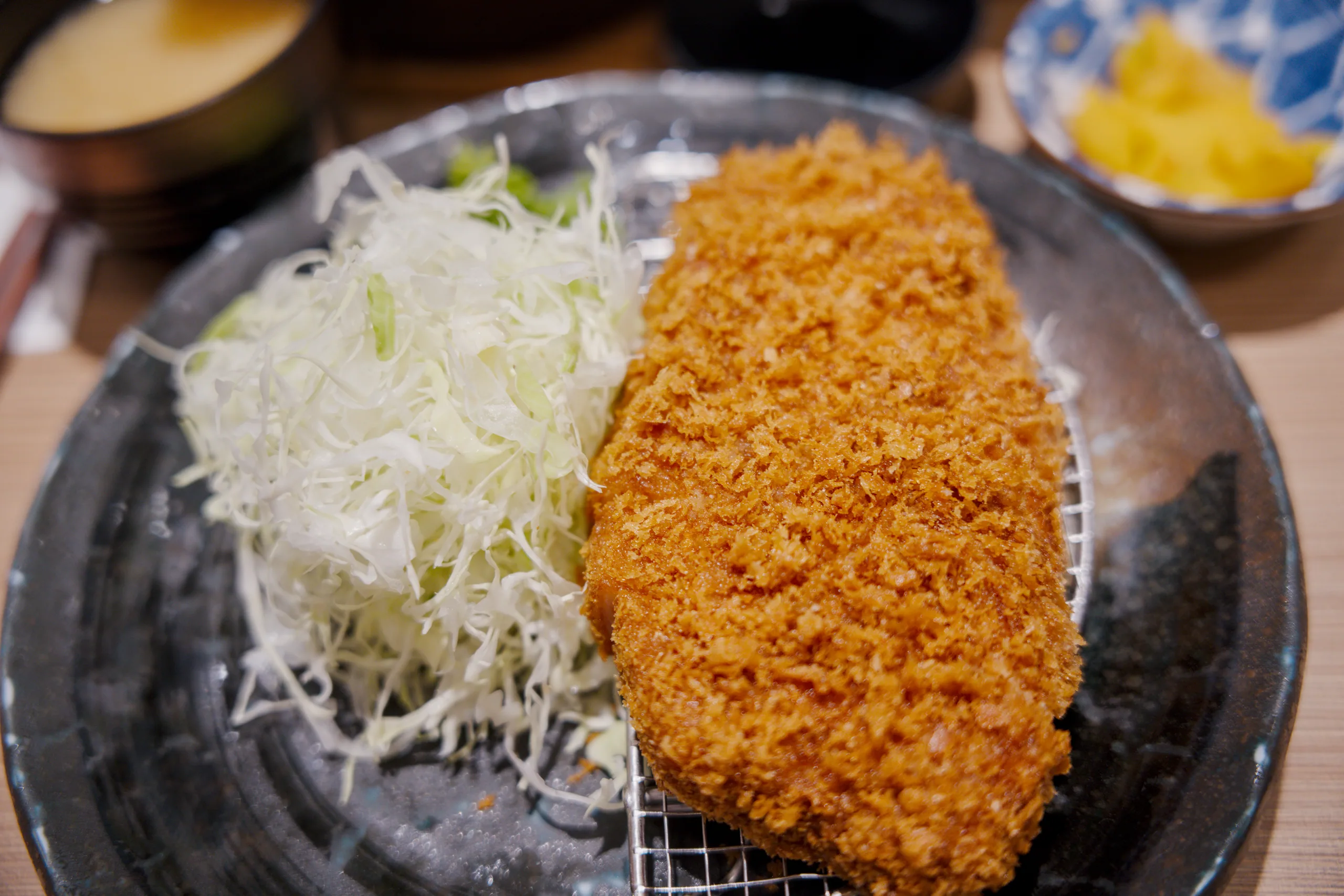 A golden-brown breaded cutlet with shredded cabbage on a dark plate.