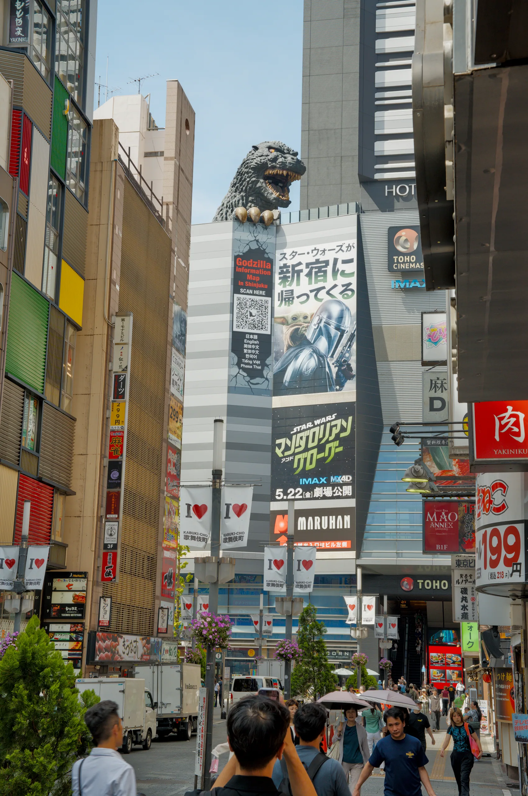 A narrow urban street flanked by tall buildings plastered with commercial signage at multiple levels.