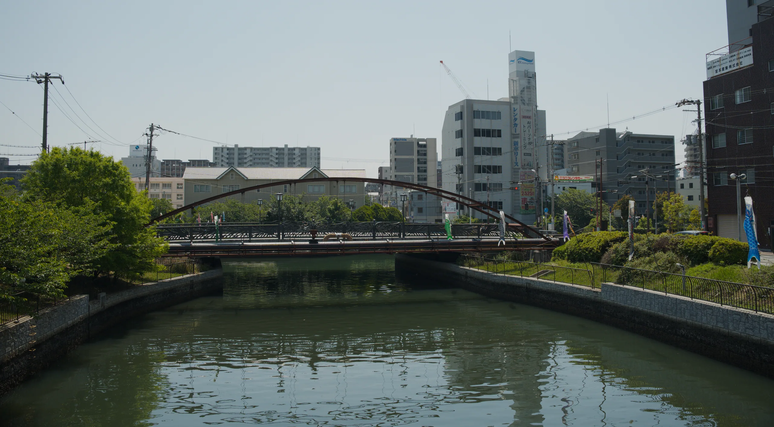 A calm urban canal runs between modern apartment buildings with a bridge visible across the distance.