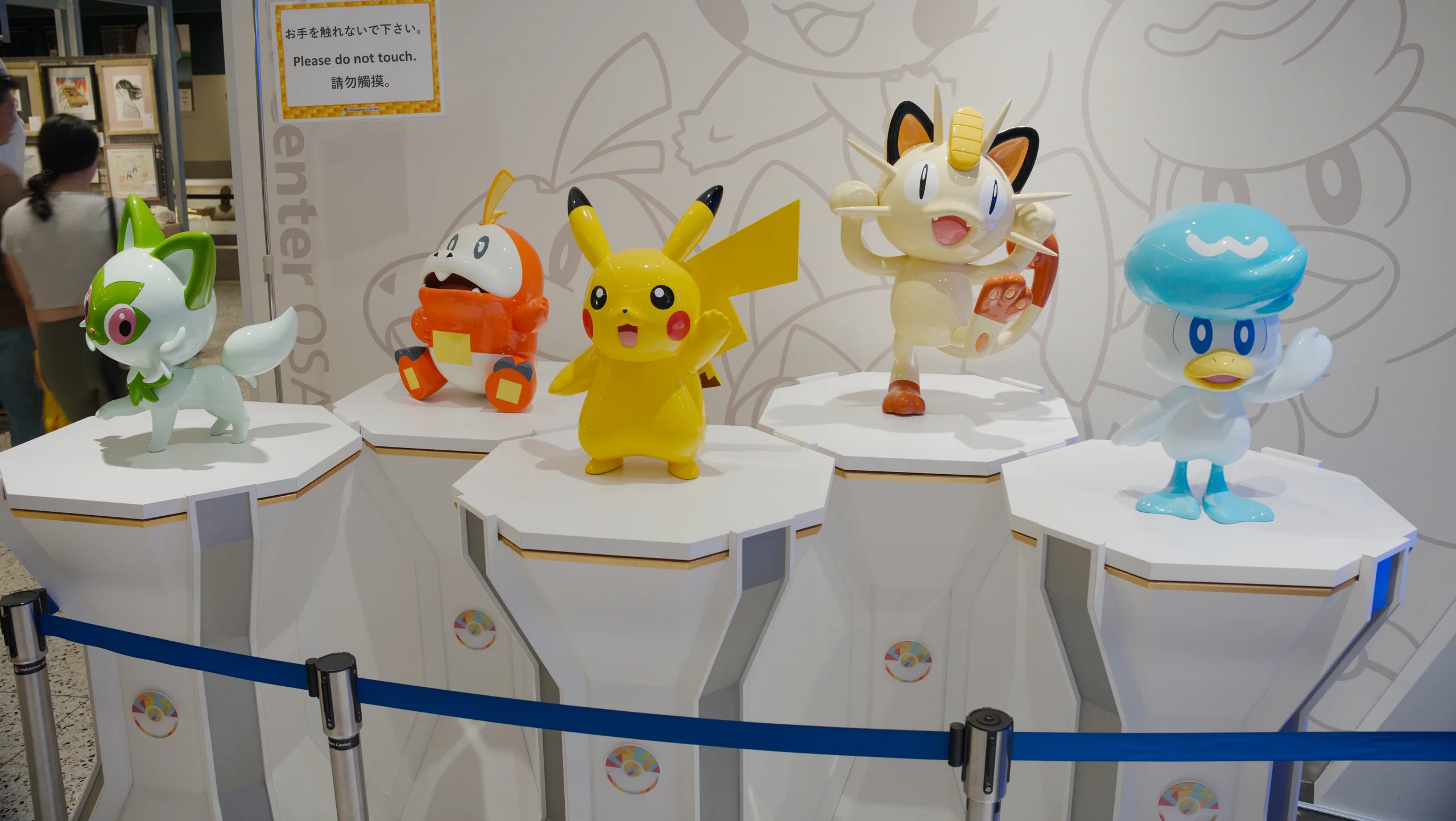Pokémon figurines displayed on white pedestals behind a blue rope barrier.