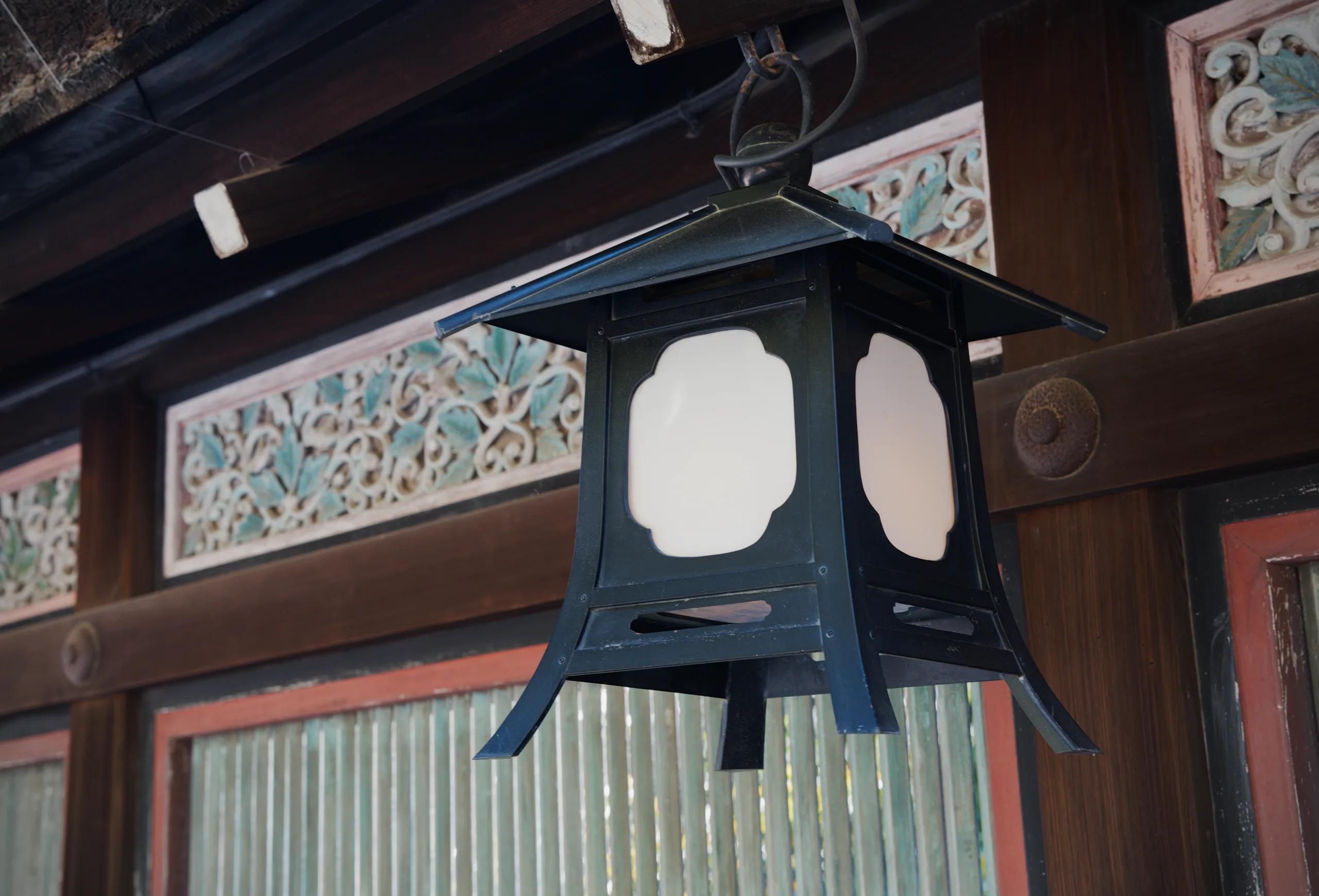 Black hanging lantern with circular windows beneath dark wooden eaves and decorative panels.