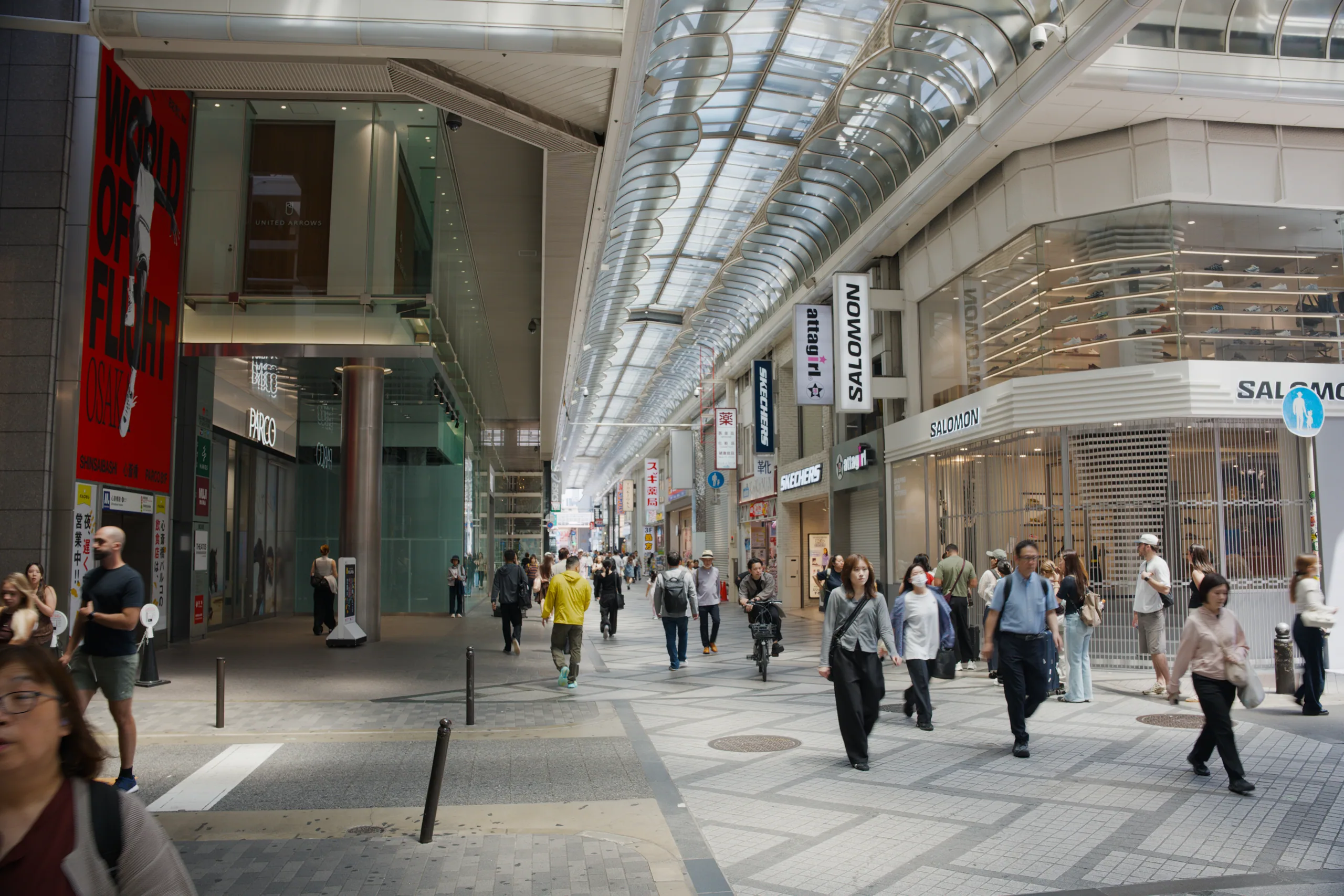 A modern covered shopping arcade with high ceilings, natural light, and scattered pedestrians.