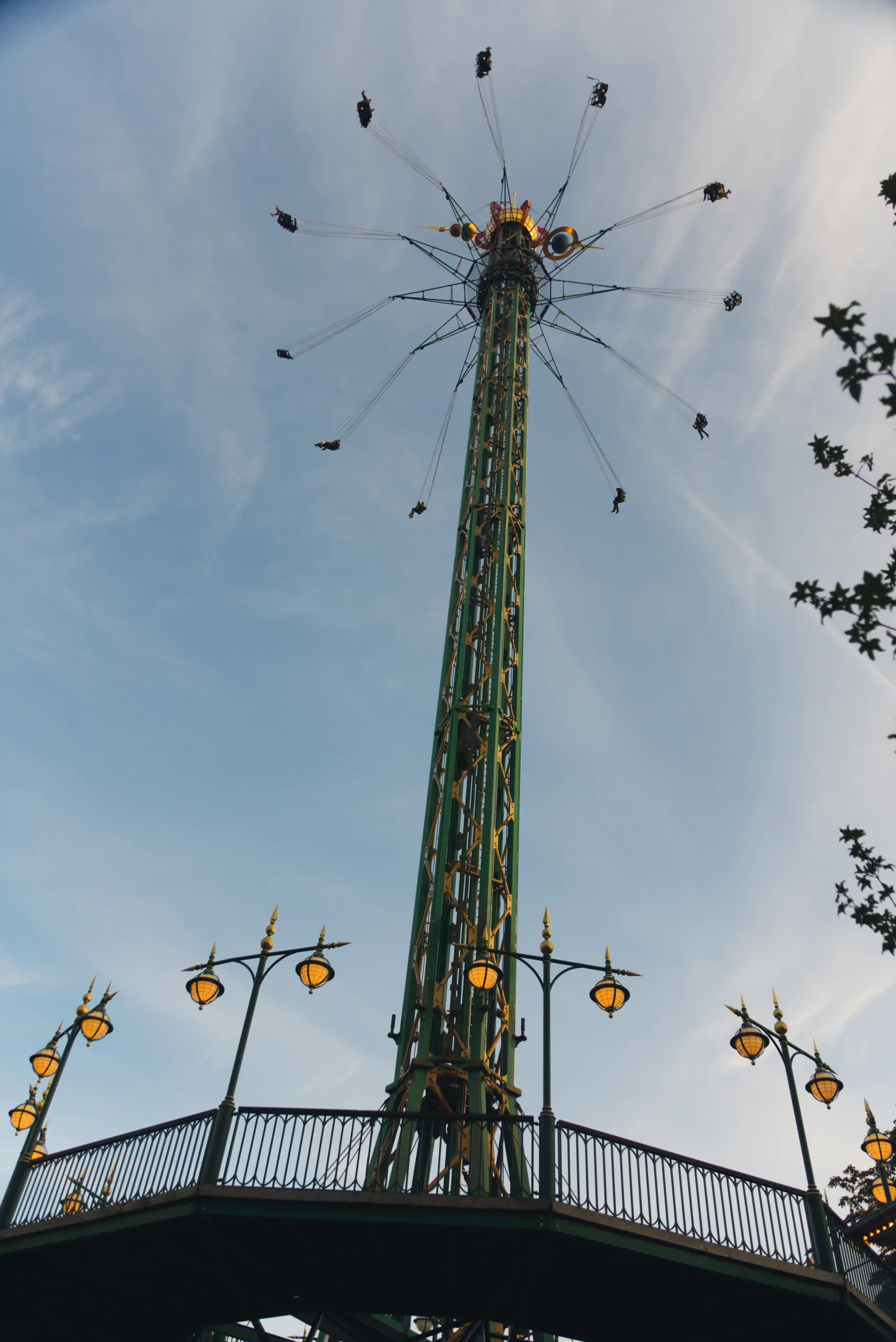 The Star Flyer swing tower at Tivoli seen from directly below, riders suspended on chains far above against a pale sky.
