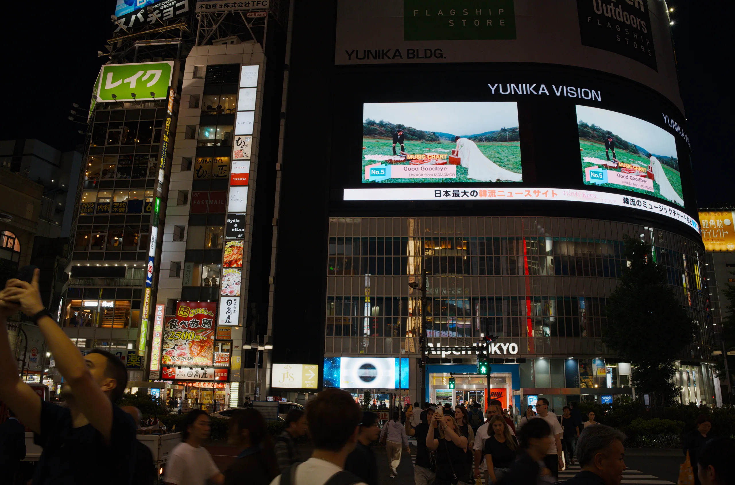 Crowded nighttime shopping street with large illuminated signs, video screens, and dense neon signage overhead.