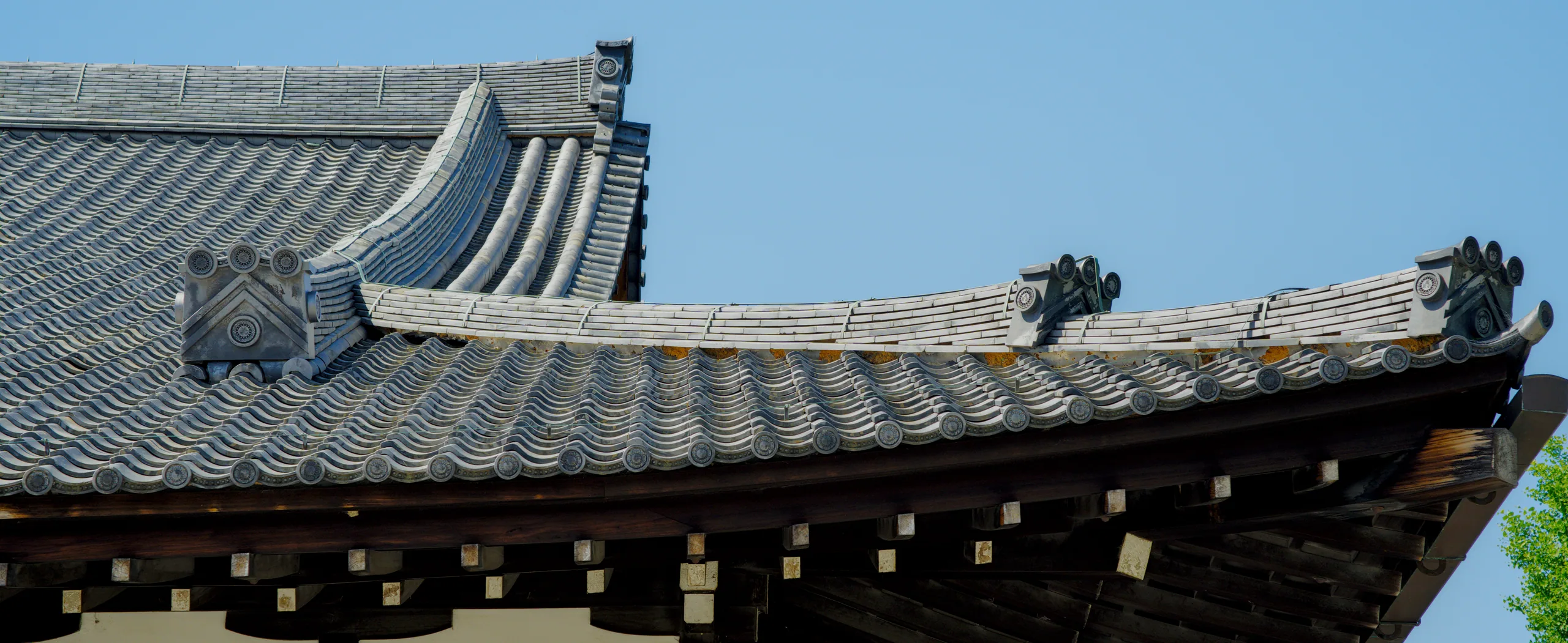 Japanese temple roof with segmented tiles and upturned eaves against clear sky.