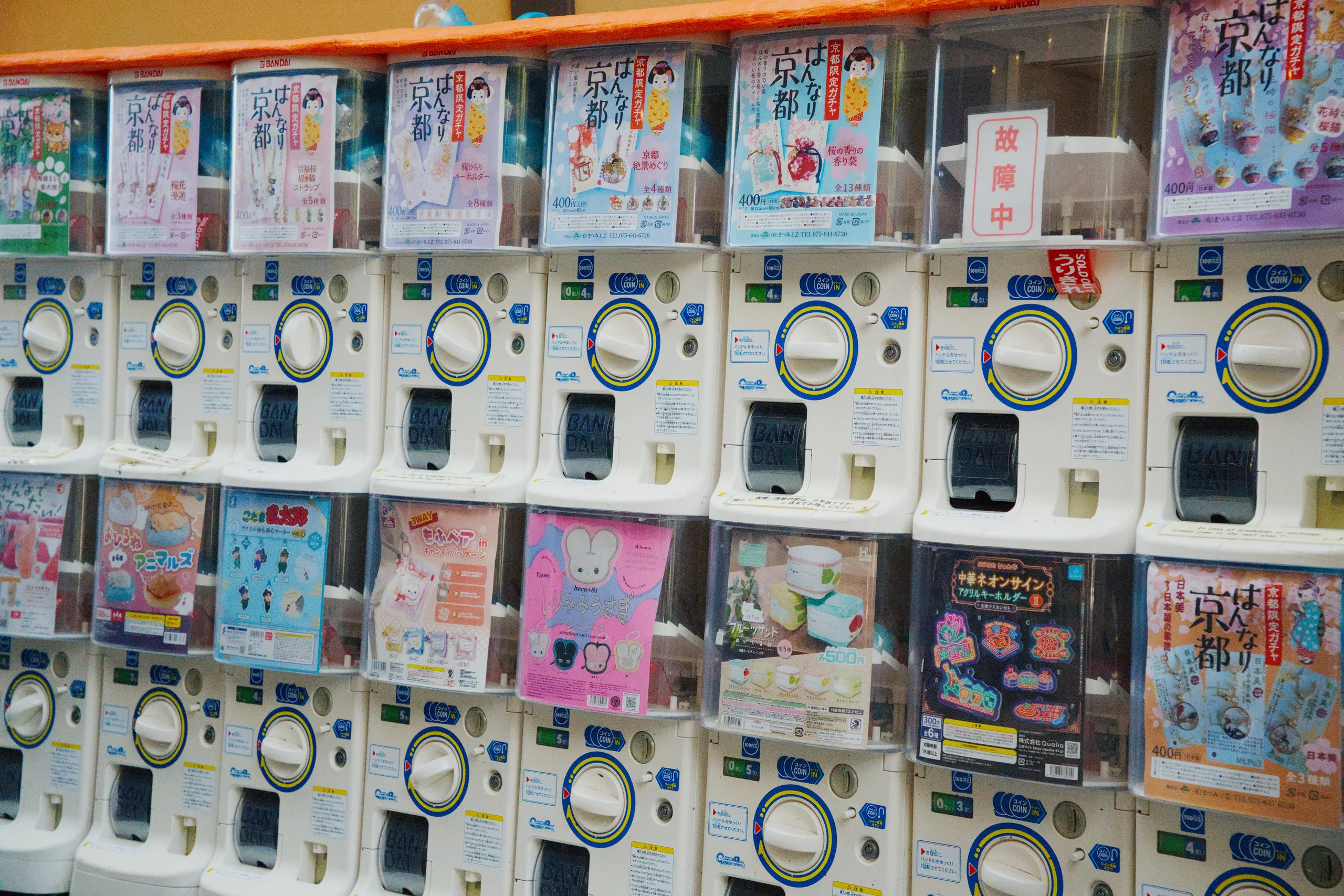 A wall of arcade and vending machines with colorful advertisements in a busy street area.