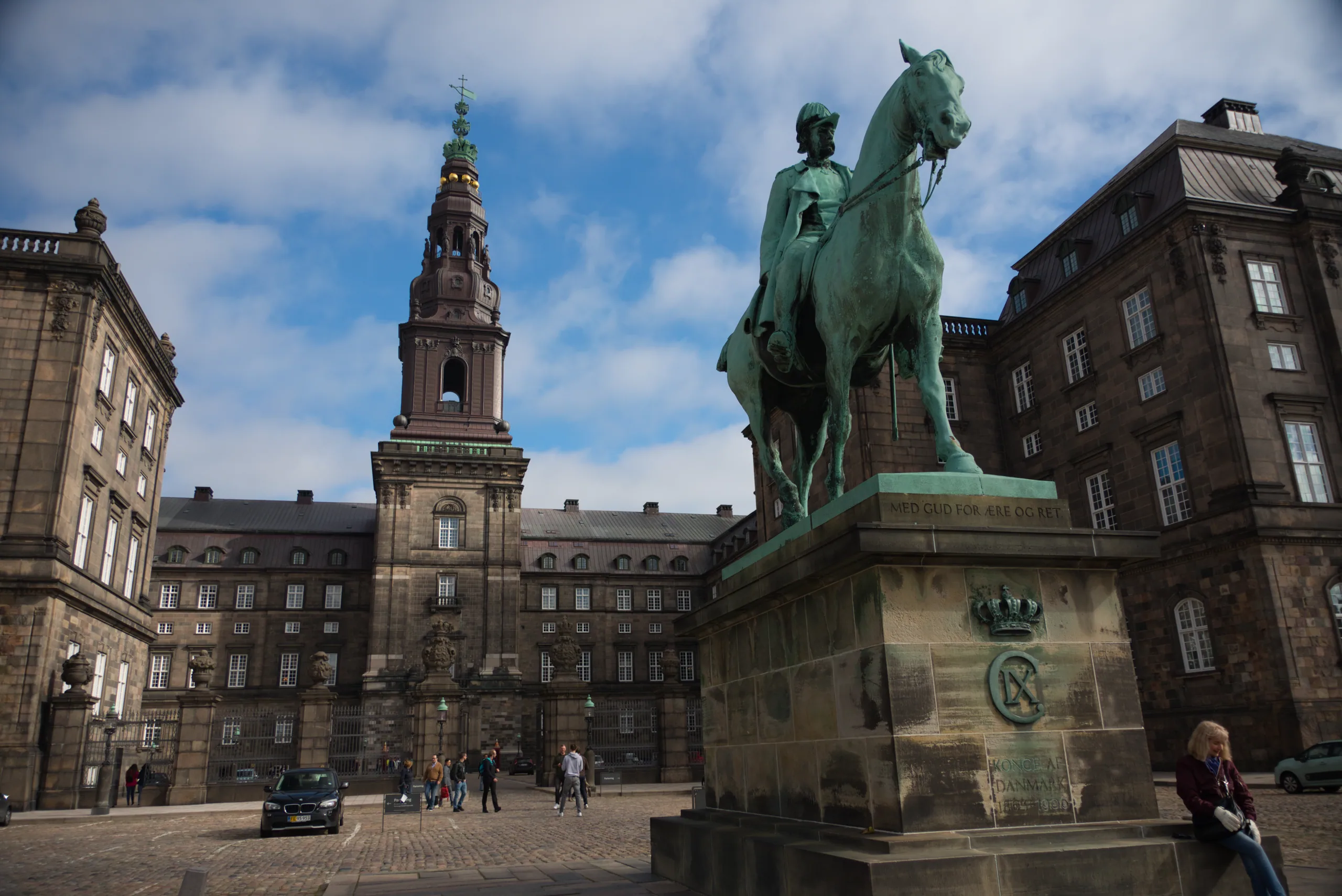 Christiansborg Palace behind a bronze equestrian statue on a stone plinth, under a bright sky with scattered cloud.