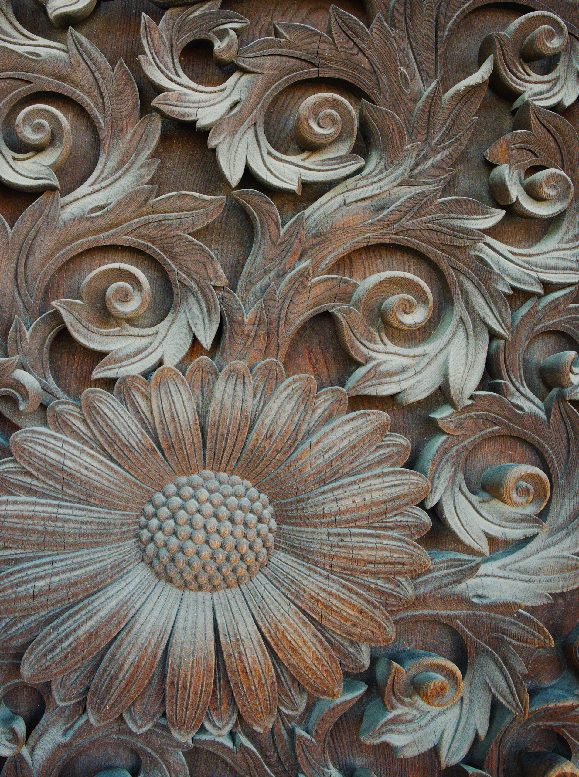 Carved wooden ornament with scrolling acanthus leaves framing a large sunflower in relief.